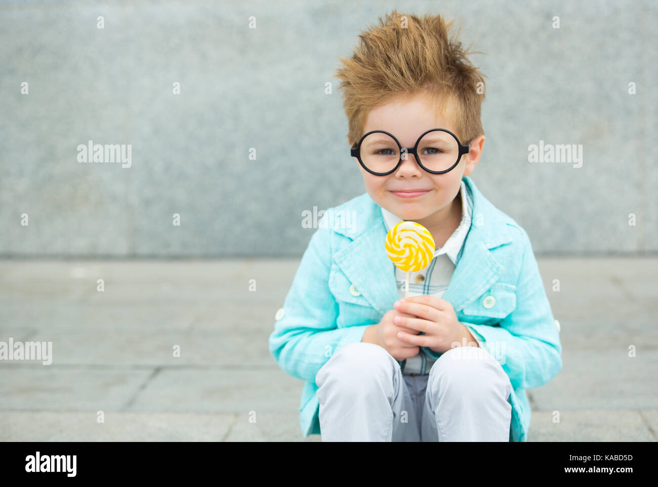 Moda bimbo in camicia di menta sorge su un muro grigio Sfondo. trendy boy lollipop permanente sulla strada. Foto Stock