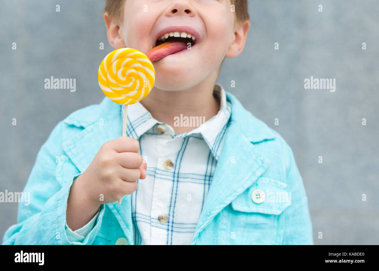 Moda bimbo in camicia di menta e sneakers sorge su un muro grigio Sfondo. trendy boy lollipop permanente sulla strada. Foto Stock