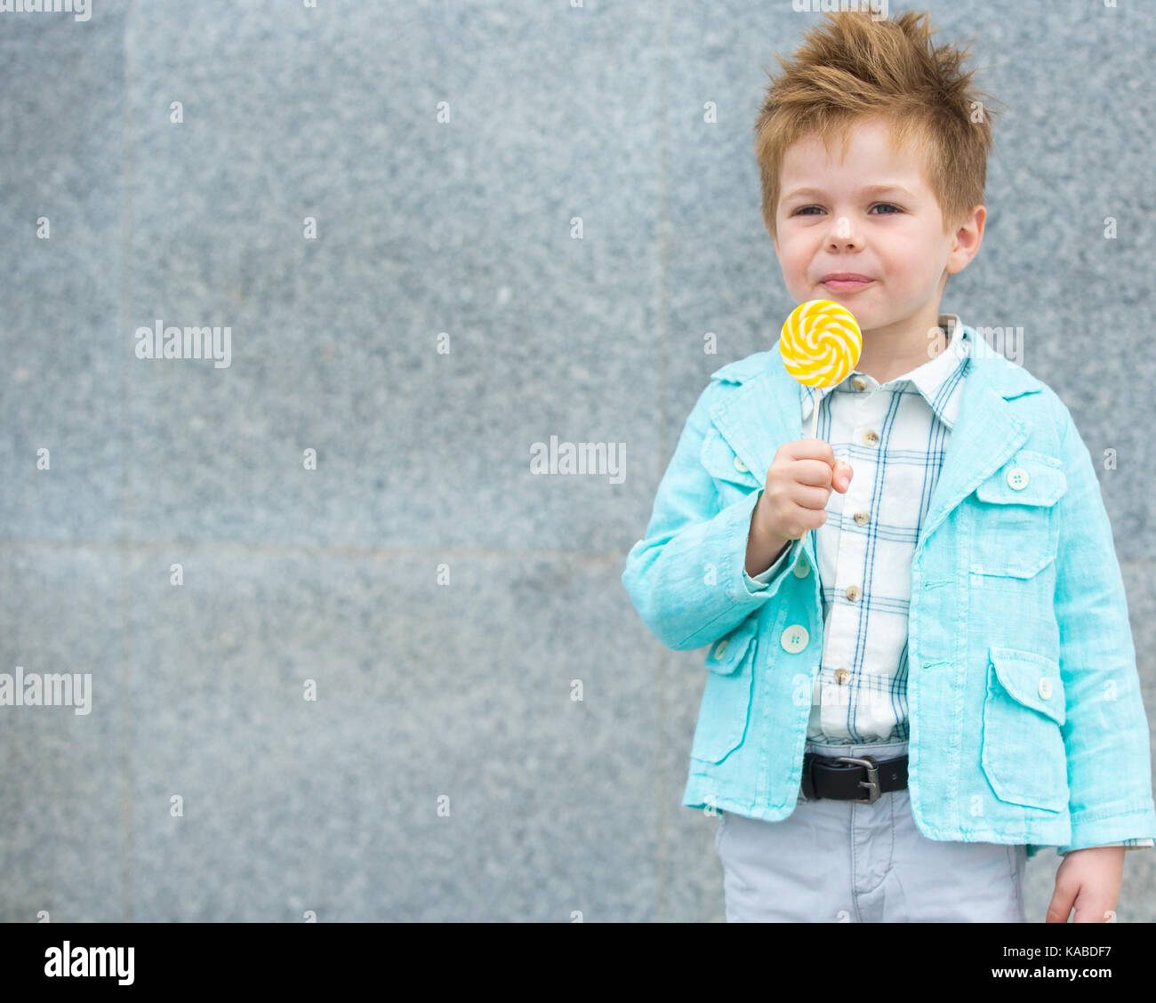 Moda bimbo in camicia di menta e sneakers sorge su un muro grigio Sfondo. trendy boy lollipop permanente sulla strada. Foto Stock