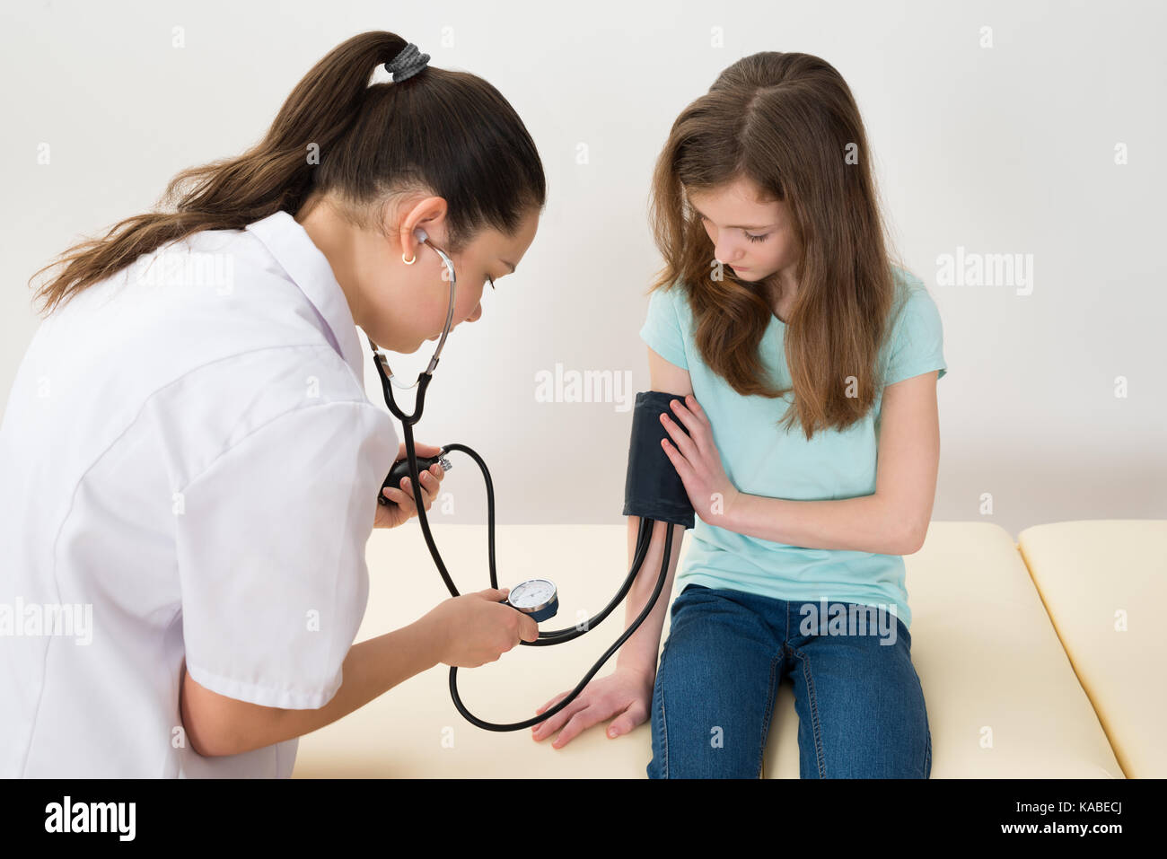 Medico donna controllando la pressione del sangue della ragazza seduta sul letto di ospedale Foto Stock