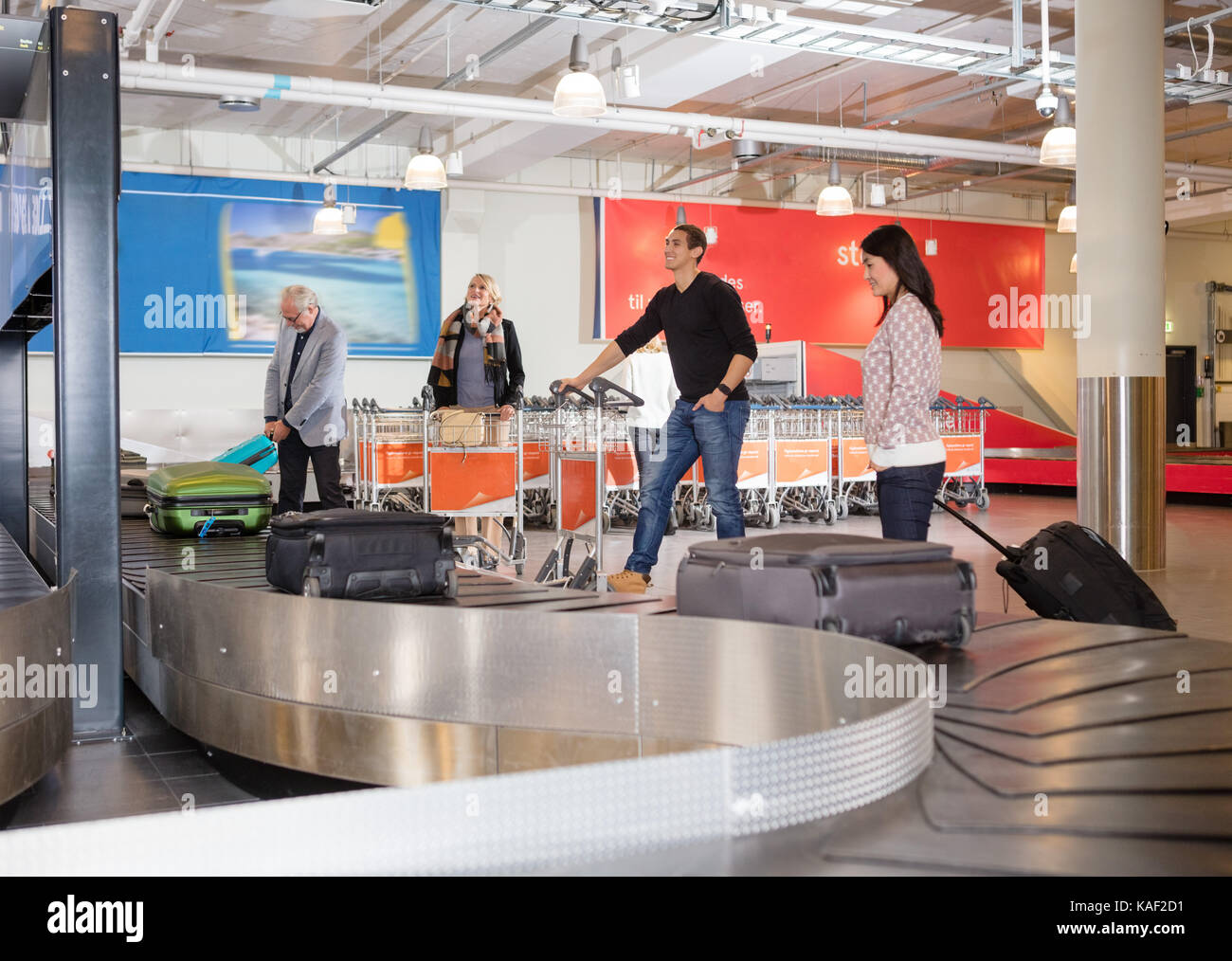 I viaggiatori in attesa per i bagagli dal nastro trasportatore in aeroporto Foto Stock