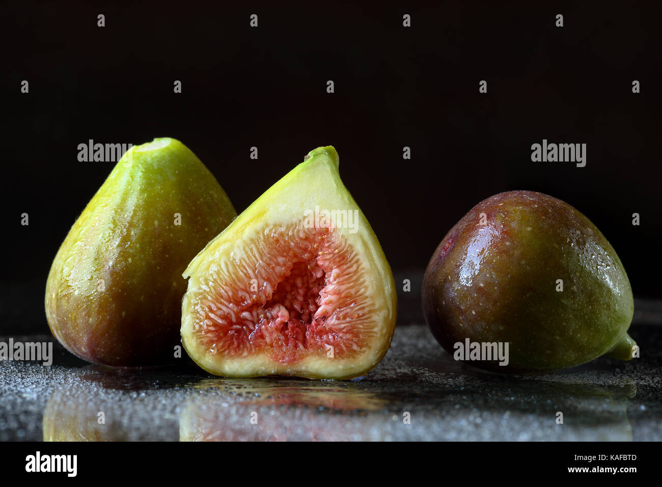 Chiudere fino a due e una metà fresche a fette fig la frutta in un umido sfondo nero con riflessi e gocce d'acqua. Macro food texture con spazio per il testo Foto Stock