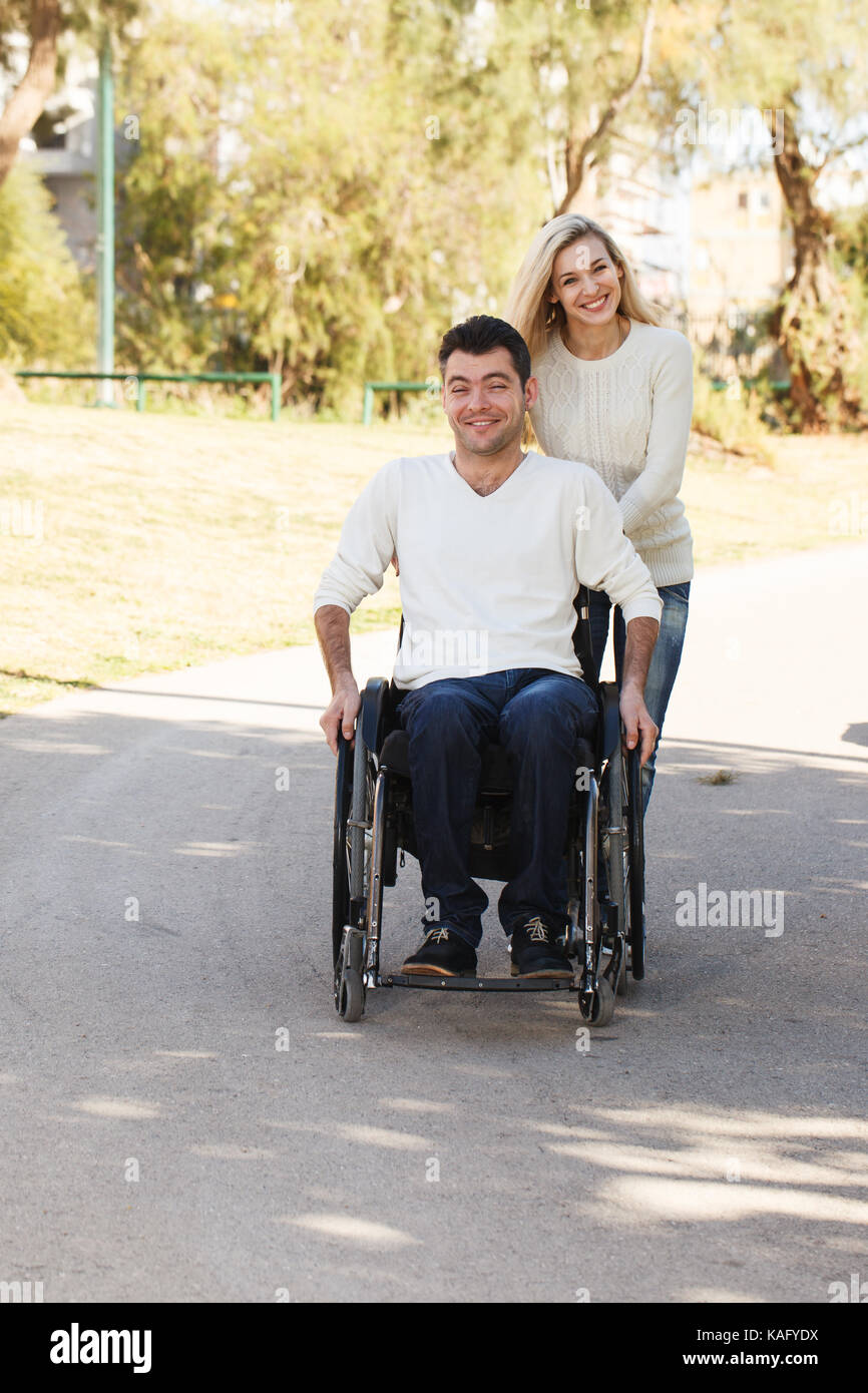 Uomo disabili su sedia a rotelle a piedi con la sua ragazza nel parco Foto Stock
