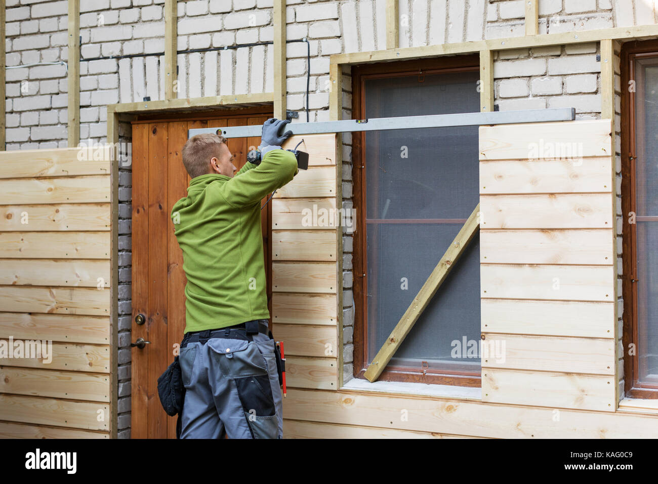 Lavoratore ripristino di vecchi mattoni casa facciata con nuove tavole di legno Foto Stock