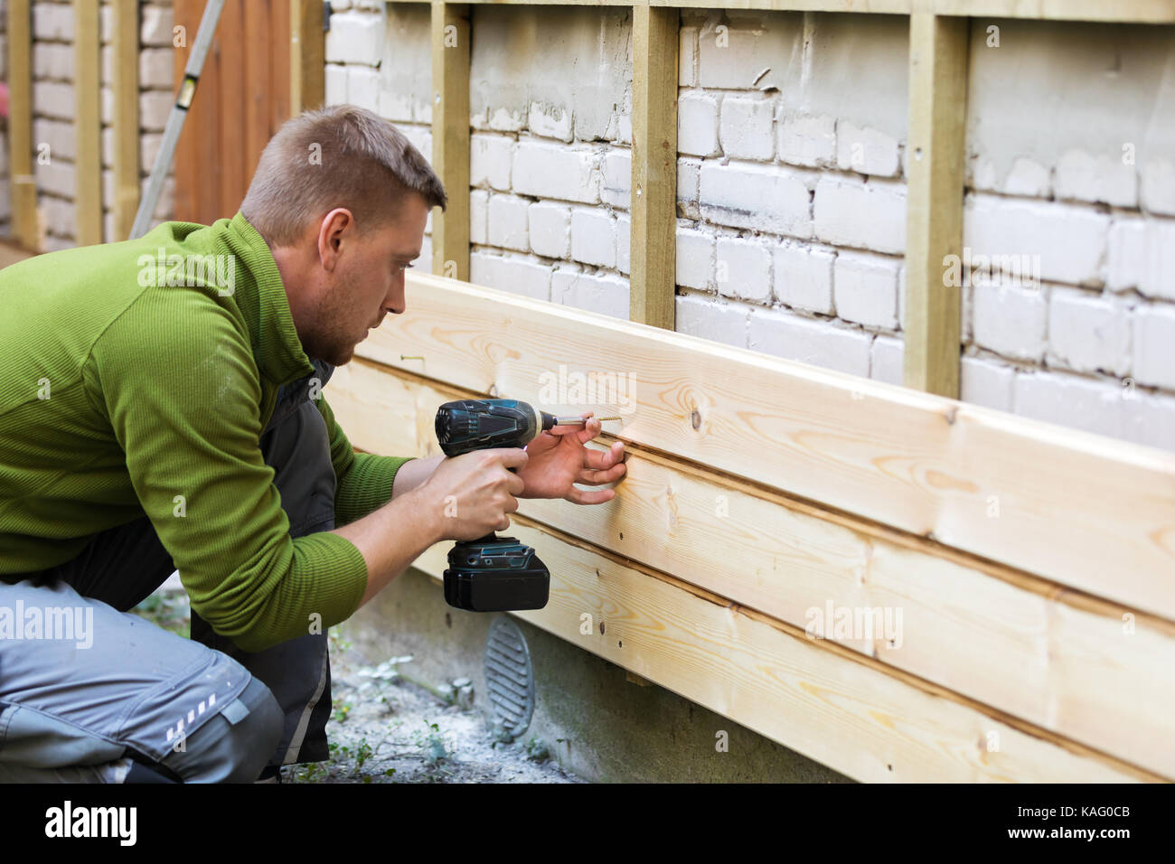 Operaio edile di installare nuove tavole di legno sulla casa vecchia facciata in mattone Foto Stock