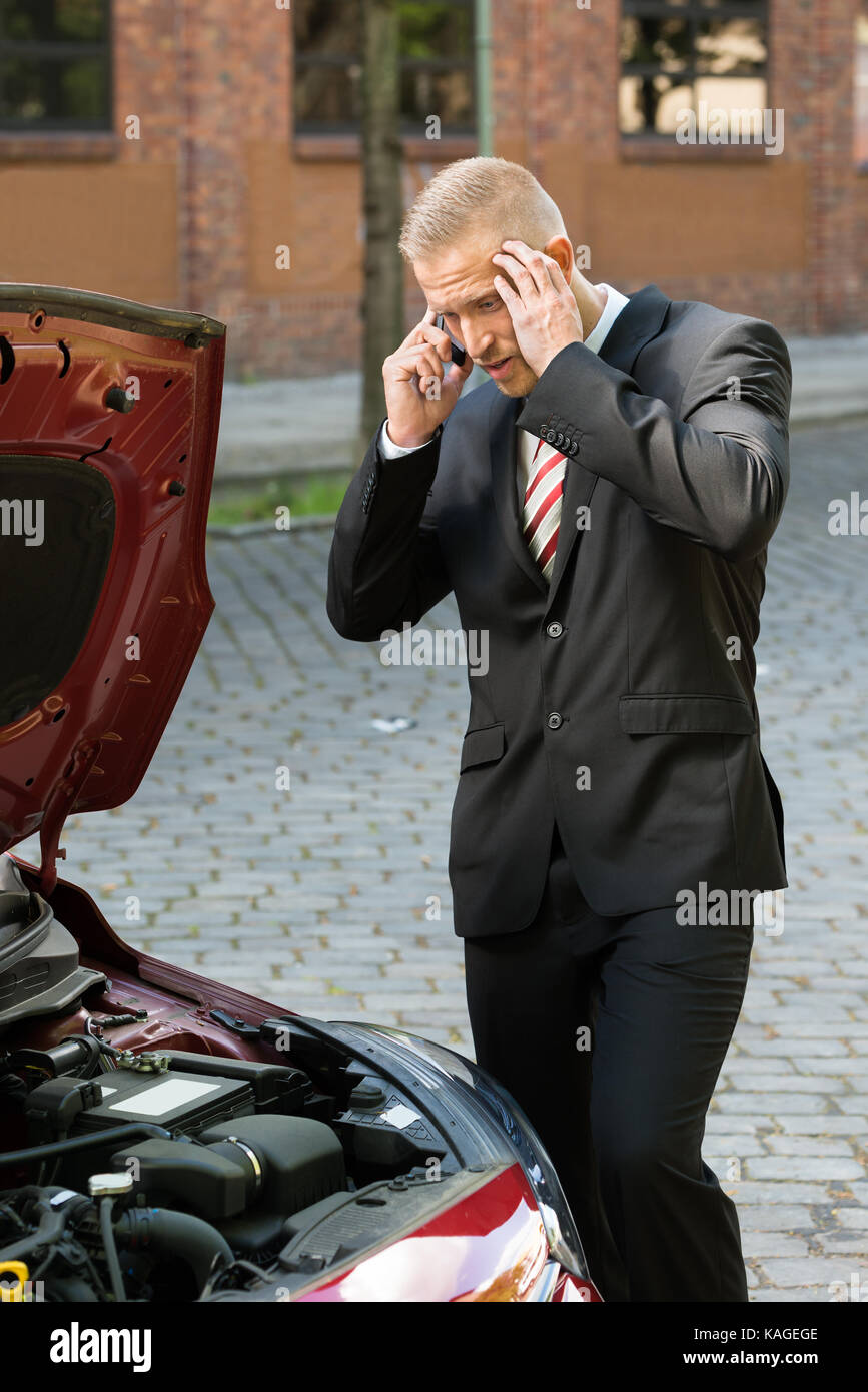 Sottolineato giovane chiamando sul cellulare per il servizio con la sua auto di rottura Foto Stock