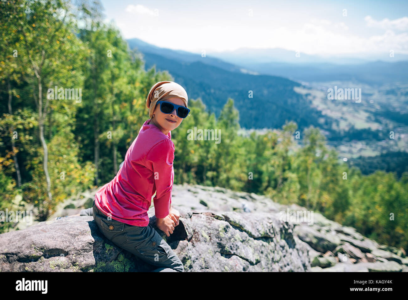 Portrat del piccolo felice ragazza seduta sulla scogliera di roccia in montagna. l'infanzia Foto Stock