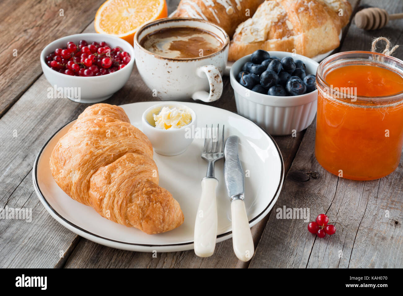 La prima colazione continentale cornetti freschi con burro, tazza di caffè, marmellata e frutta su un tavolo di legno. primo piano, orizzontale Foto Stock