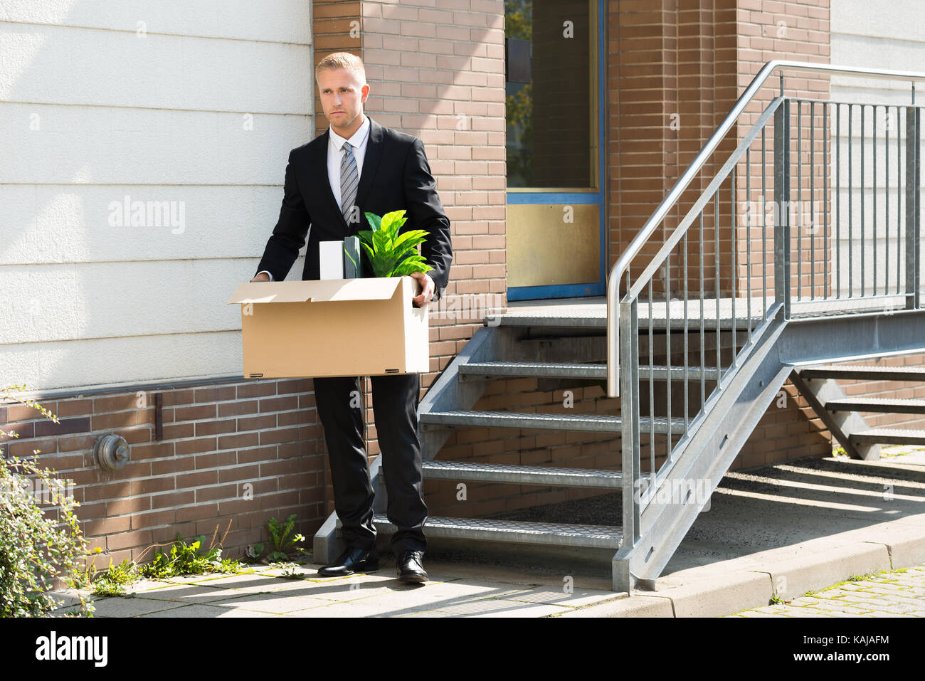 Imprenditore deluso in piedi con la scatola di cartone al di fuori ufficio Foto Stock
