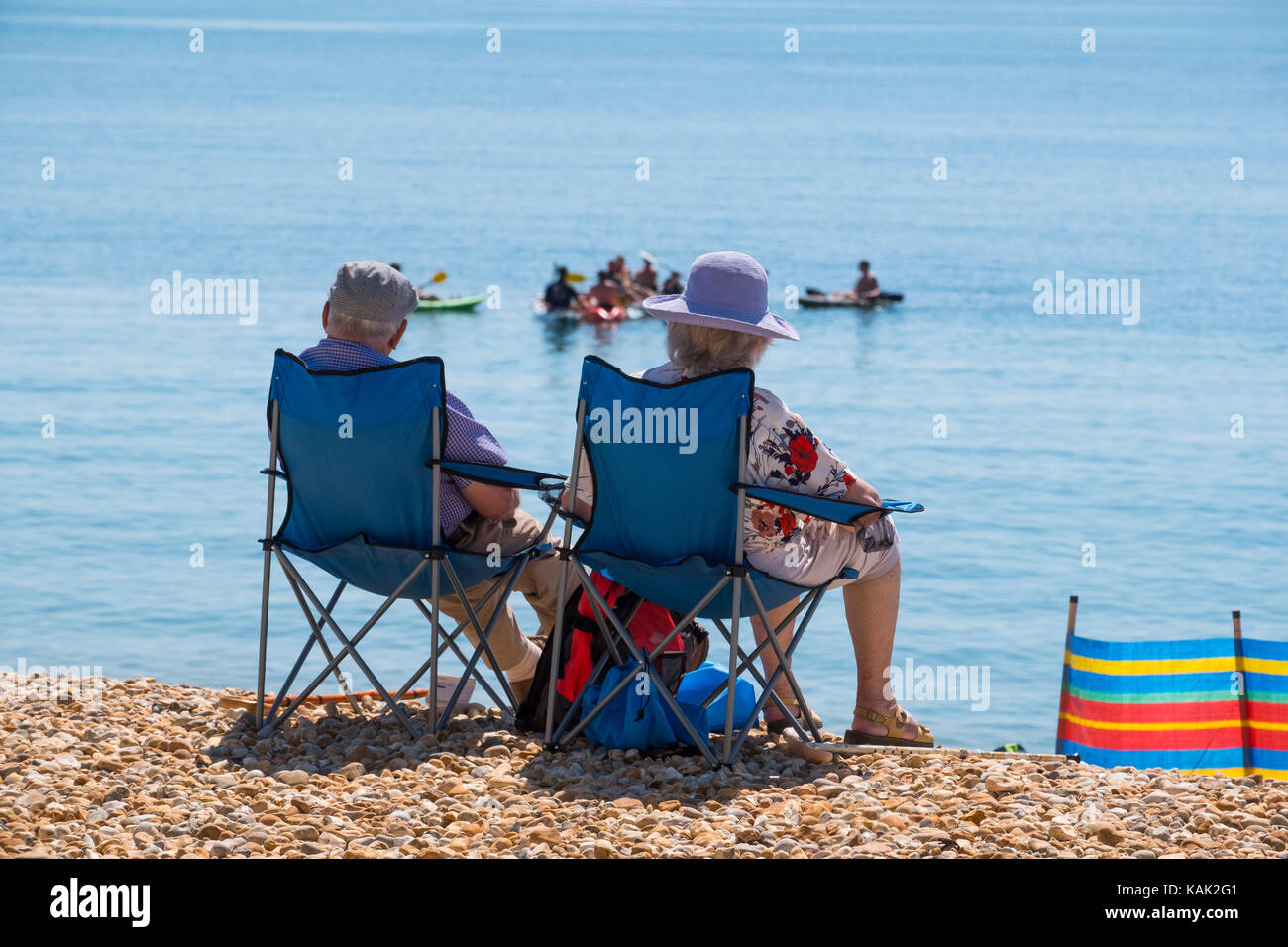 Anziani uomo e donna seduta sulla spiaggia a Lyme Regis, Dorset, Regno Unito. Foto Stock