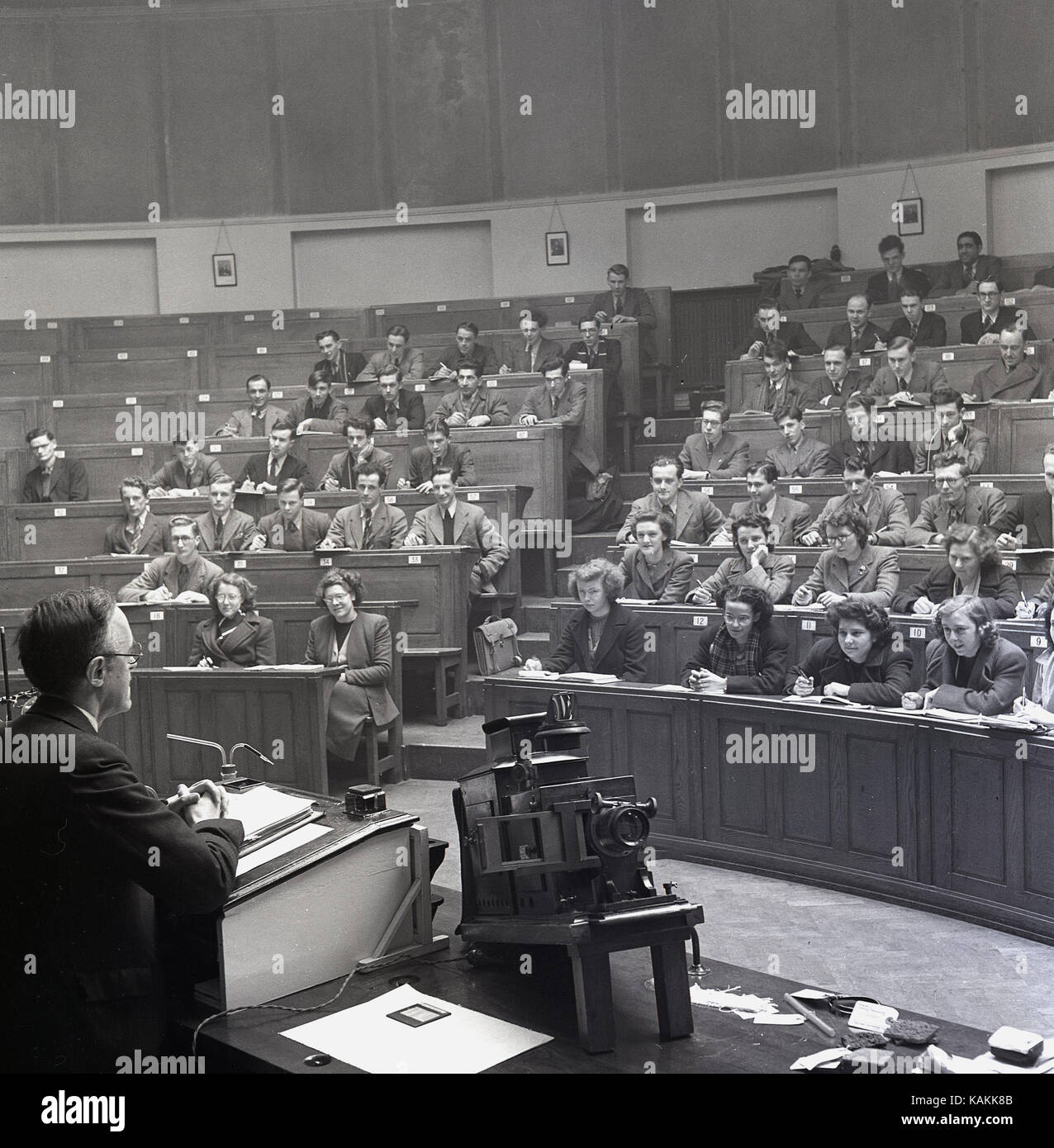 Degli anni Cinquanta, elegantemente vestito studenti universitari che frequentano una classe data da un maschio di professore presso l ambone in chimica principale teatro lezione all Università di Leeds, Leeds, Inghilterra, Regno Unito. Foto Stock