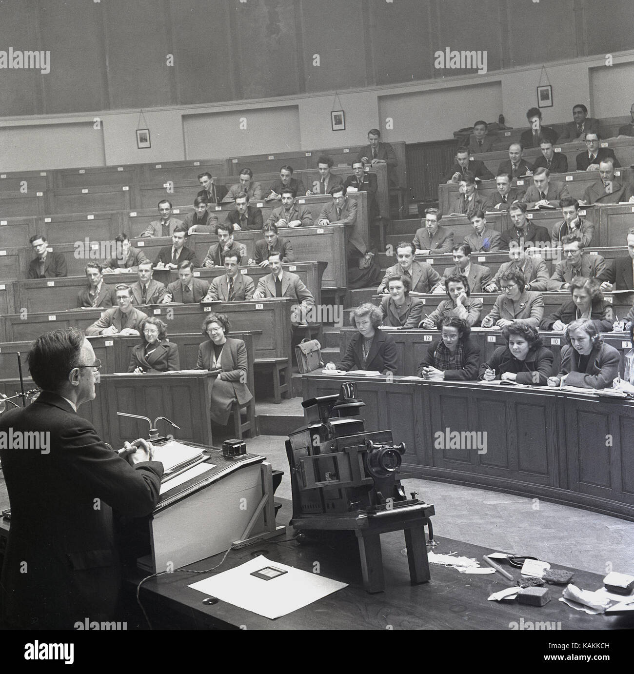 Degli anni Cinquanta, elegantemente vestito studenti universitari che frequentano una classe data da un maschio di professore presso l ambone in chimica principale teatro lezione all Università di Leeds, Leeds, Inghilterra, Regno Unito. Foto Stock