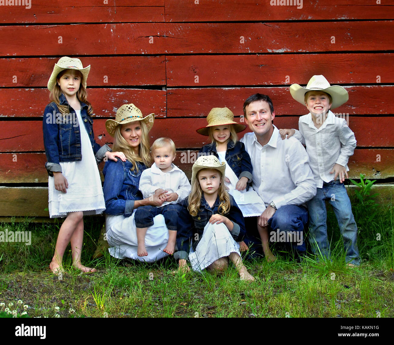 Famiglia di sette rappresentano oltre il rosso, granaio in legno. le  femmine sono indossare giubbotti denim e cappelli da cowboy. maschi sono i  jeans e camicie bianche Foto stock - Alamy