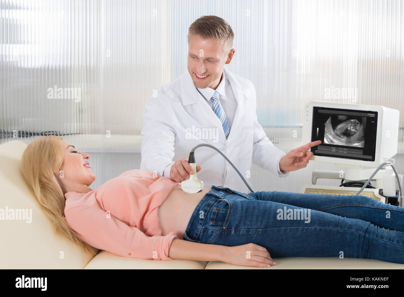 Medico maschio muovendo il trasduttore di ultrasuoni sulla donna incinta la pancia mentre guardando lo schermo in ospedale Foto Stock
