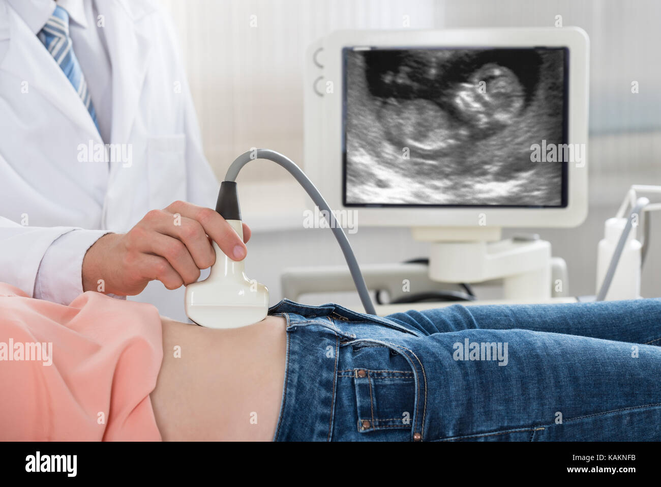 Immagine ritagliata del medico maschio muovendo la sonda ecografica sulla donna incinta il ventre Foto Stock