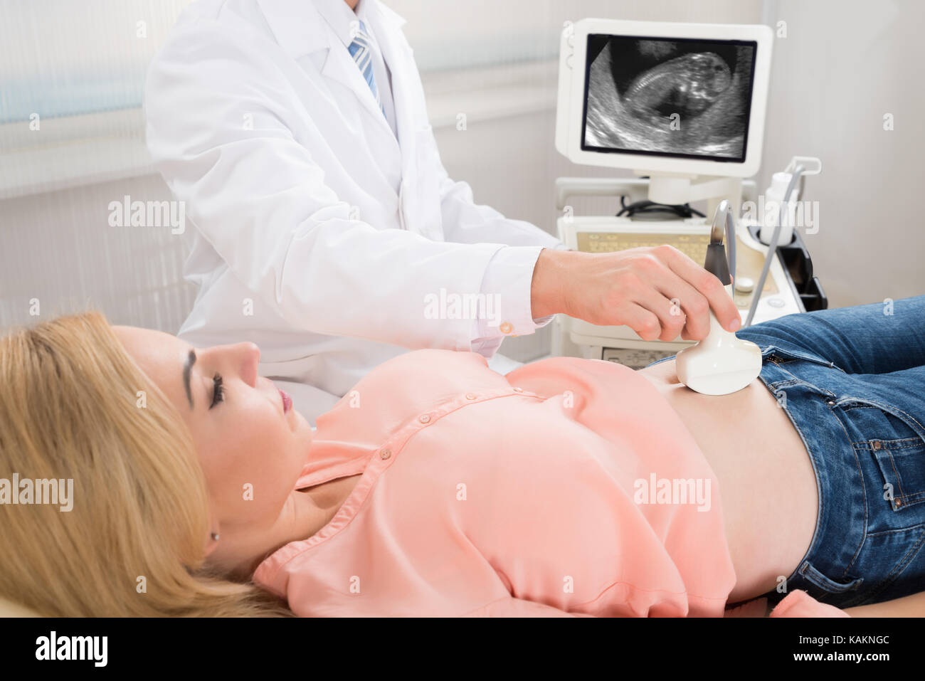 Immagine ritagliata del medico maschio muovendo il trasduttore di ultrasuoni sulla donna incinta lo stomaco Foto Stock