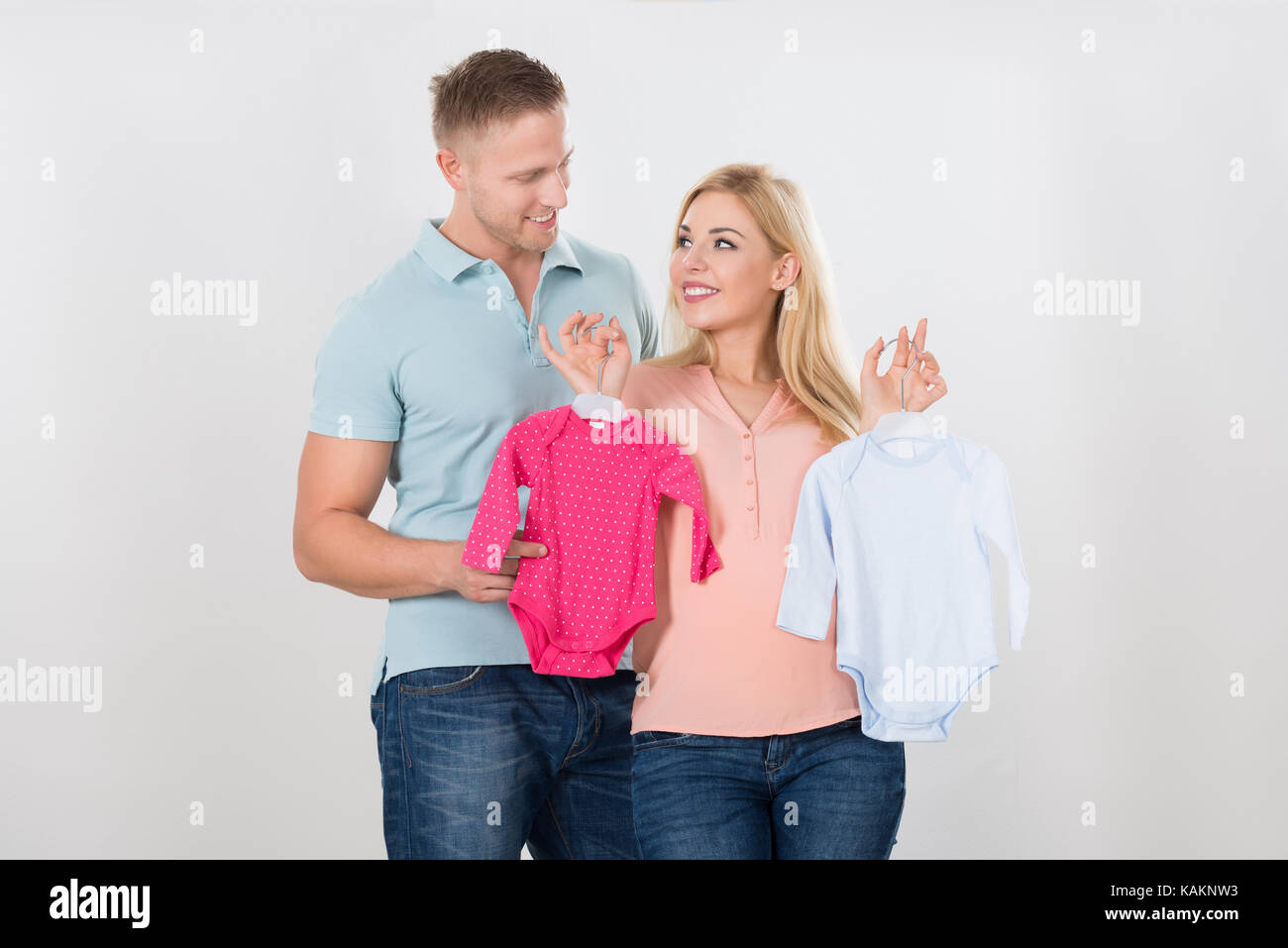 Coppia sorridente guardando ogni altra tenendo i vestiti del bambino su sfondo bianco Foto Stock