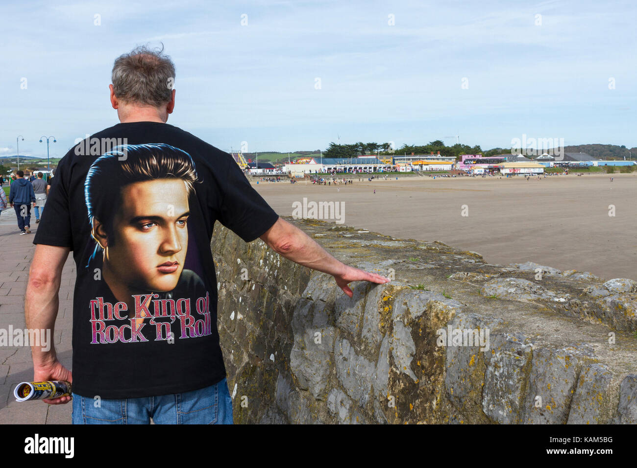 Uomo che indossa un Elvis Presley t-shirt cammina verso la Porthcawl festival di Elvis a Sandy Bay, Porthcawl, Galles Foto Stock