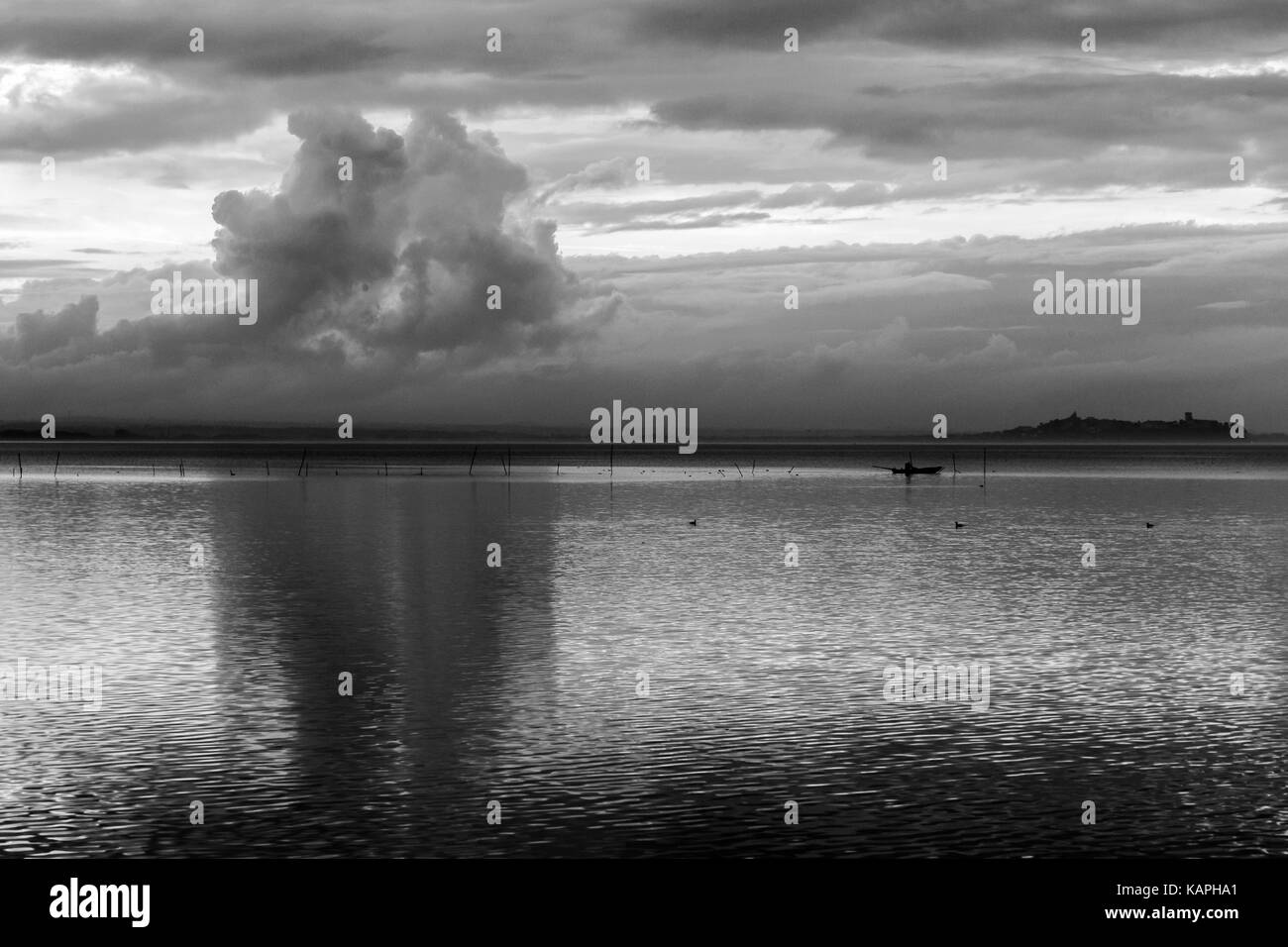 Un lago al tramonto, con belle nubi riflessi e distante un pescatore su una piccola barca Foto Stock