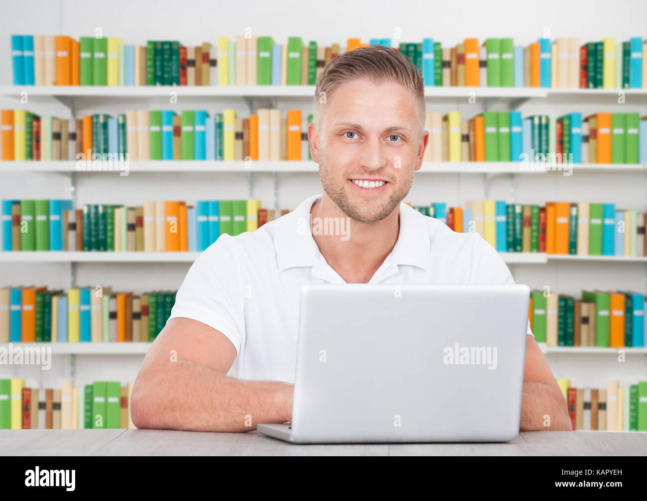 Ritratto di felice degli studenti di sesso maschile seduto con il computer portatile alla reception in libreria Foto Stock