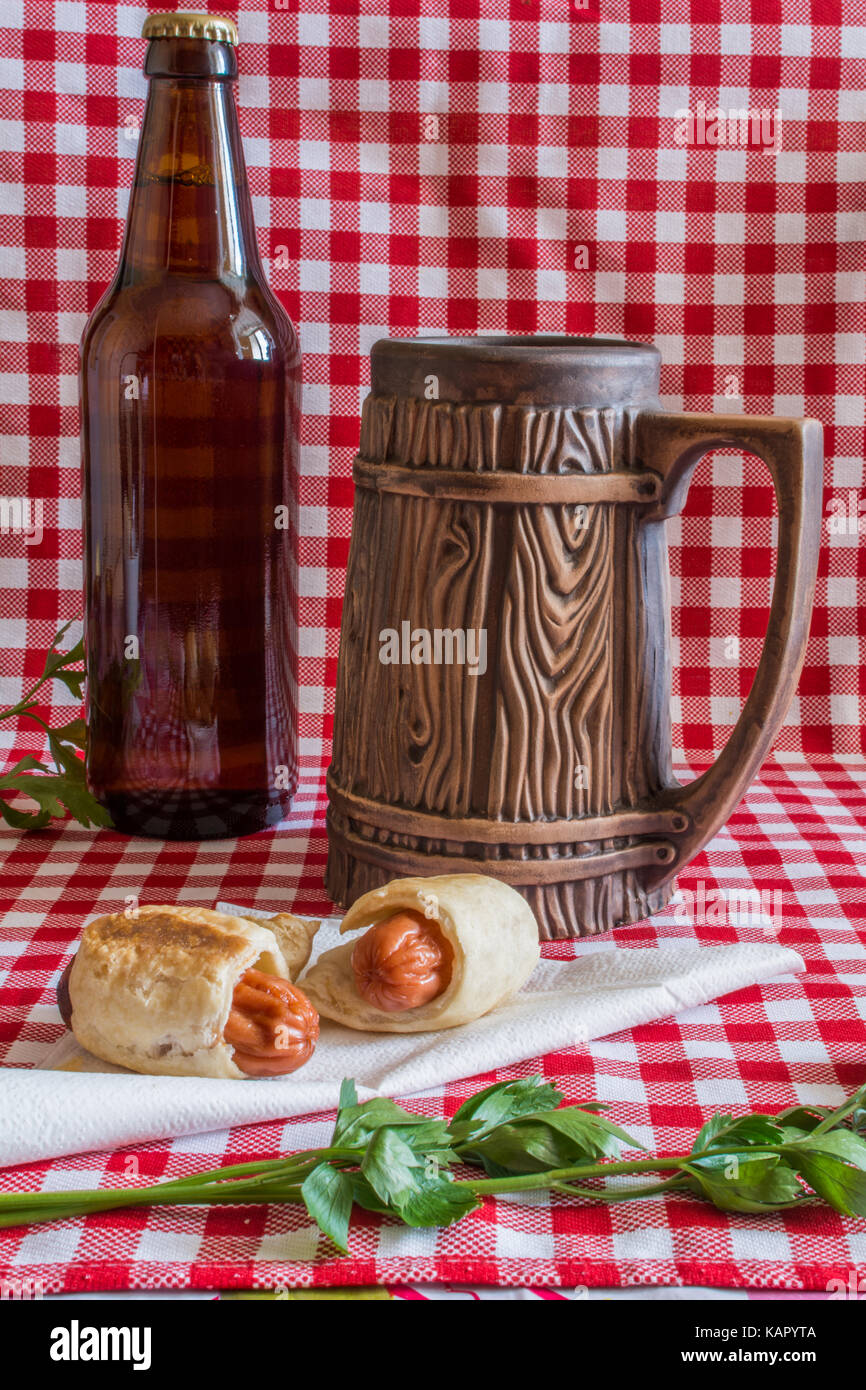 In casa mini hot dogs (salsiccia in pasticceria) su igienico con una bottiglia di birra scura e vaso di terracotta su un plaid sfondo Foto Stock