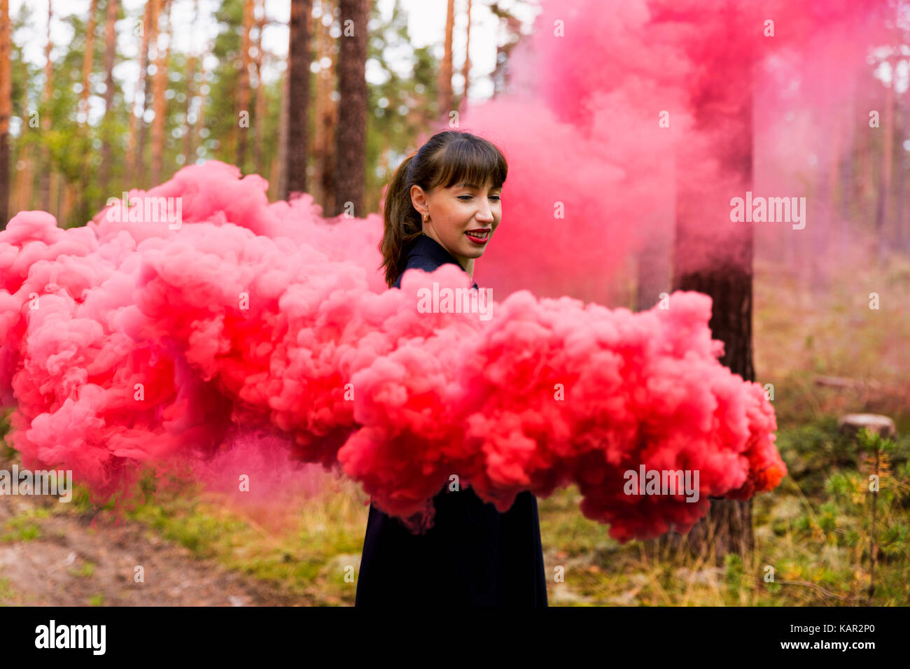 Giovane donna nella foresta divertendosi con fumo di colore rosso granata, bomba Foto Stock