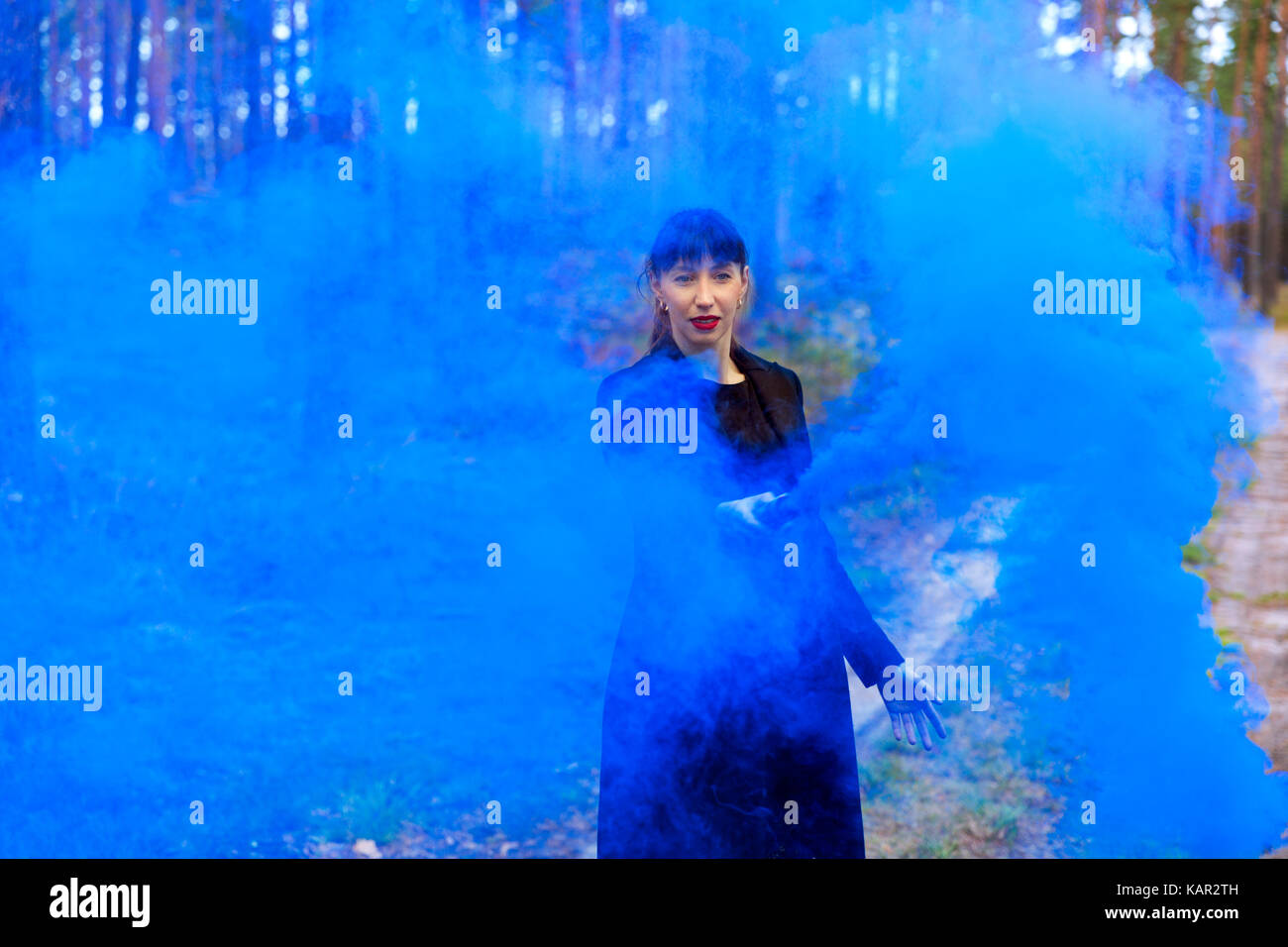 Giovane donna nella foresta divertendosi con fumo blu granata, bomba Foto Stock