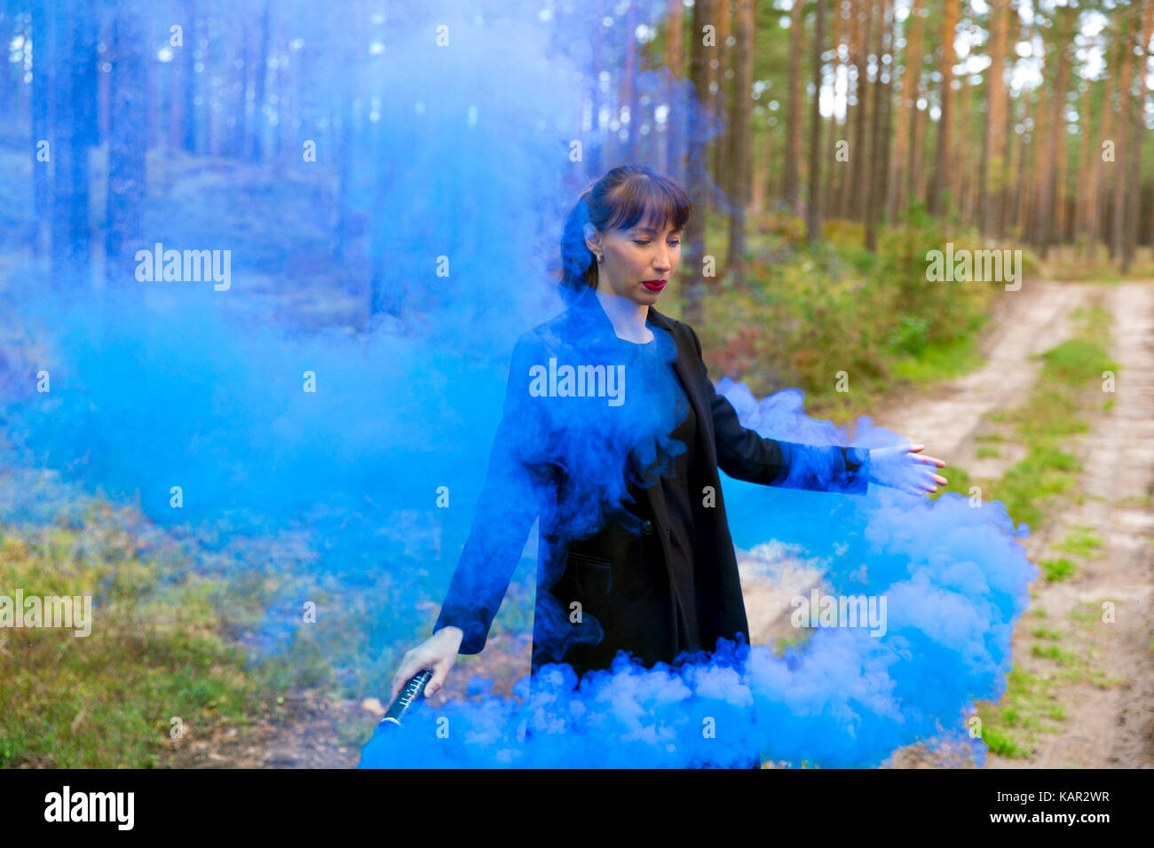 Giovane donna nella foresta divertendosi con fumo blu granata, bomba Foto Stock