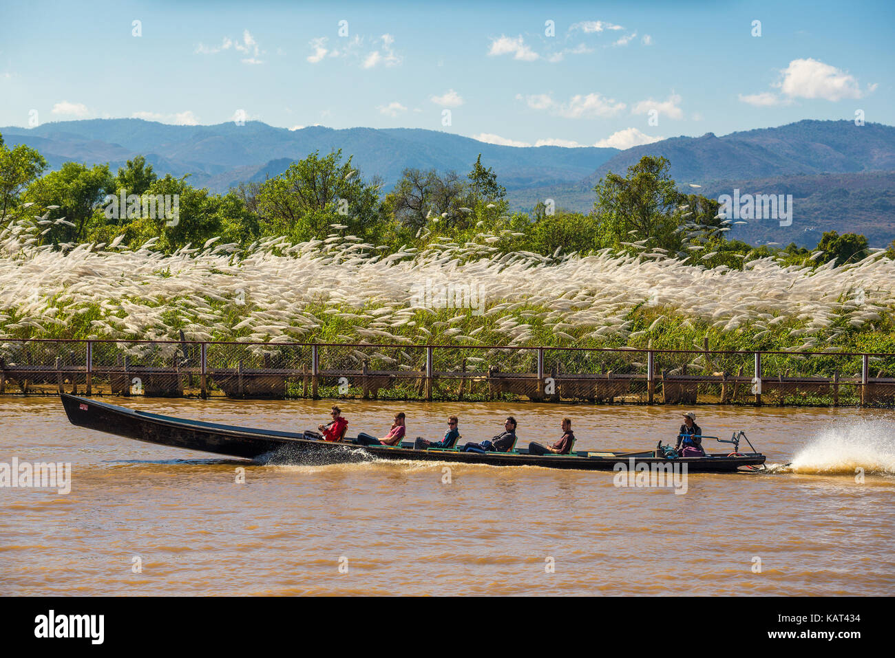 Turisti viaggiano in una barca dalla lunga coda attraverso villaggi locali in Myanmar Foto Stock