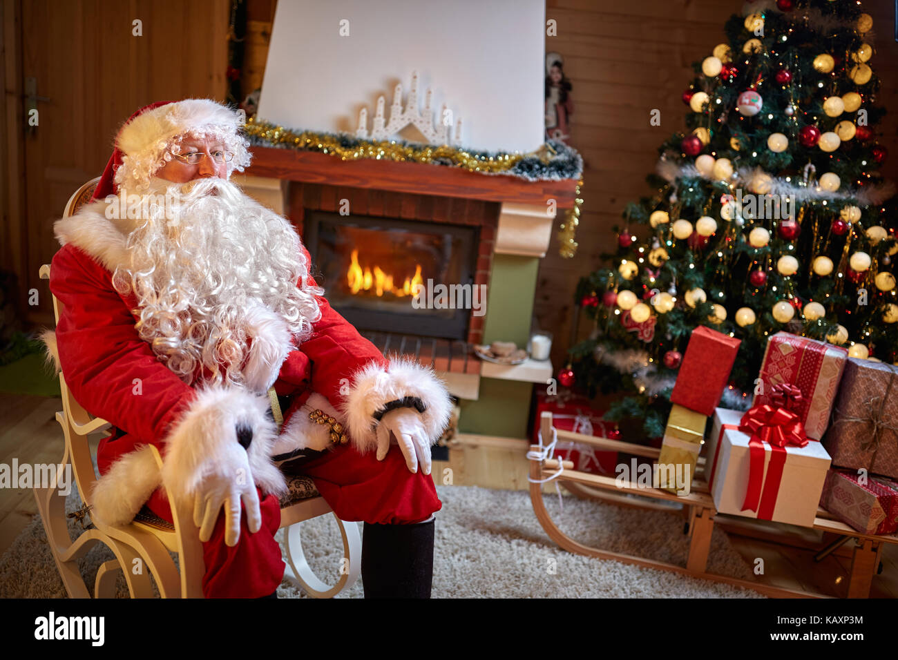 Babbo Natale seduto in camera arredata vicino al camino e albero di natale Foto Stock