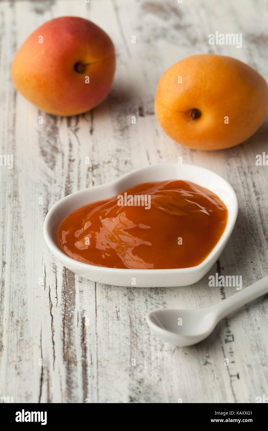 Ciotola con marmellata di albicocca fatta in casa e frutta fresca sullo sfondo Foto Stock