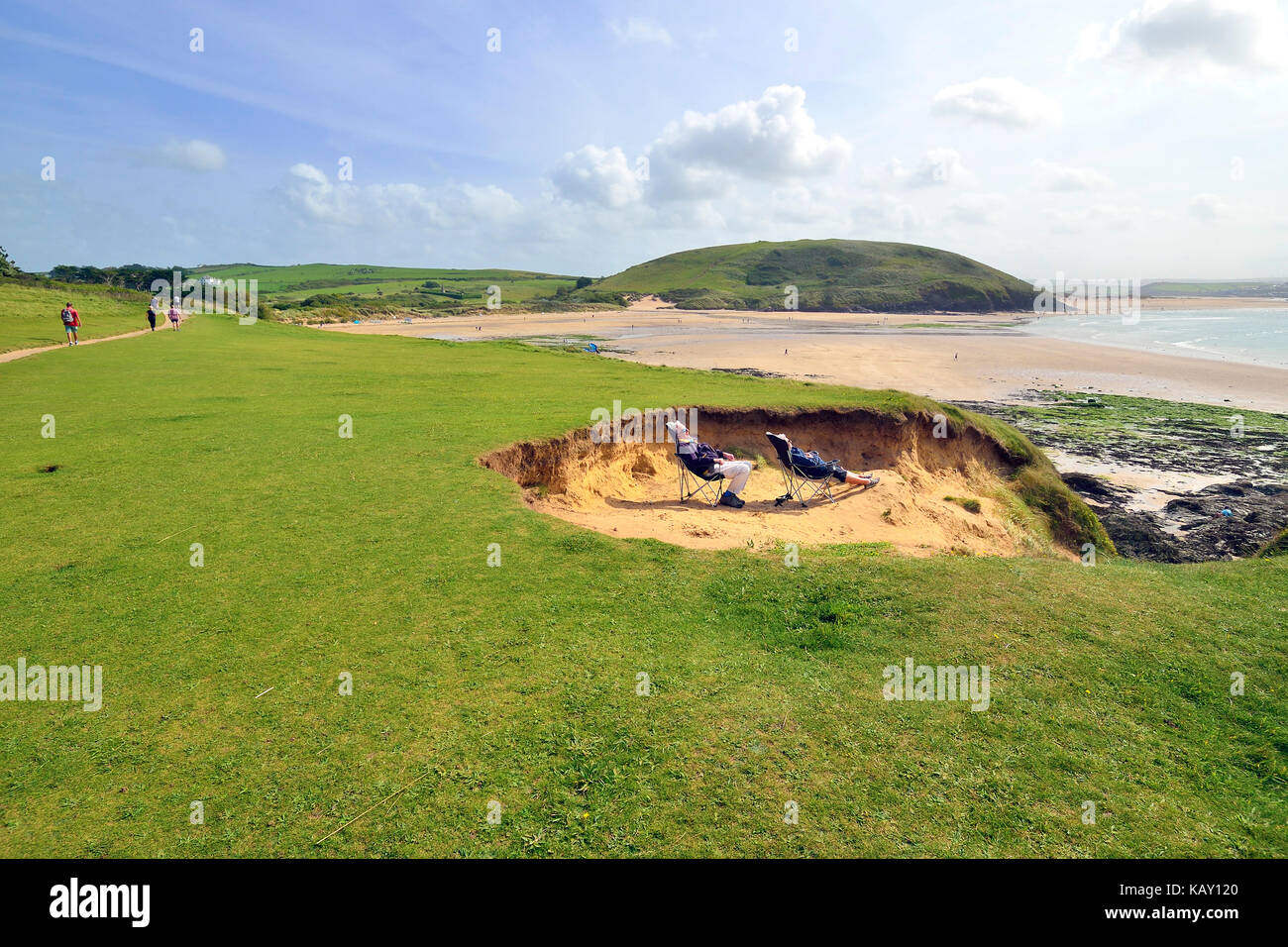 Uomo maturo e la donna riparo dal vento nelle dune di sabbia mentre crogiolandovi sotto i raggi del sole all'Daymer Bay, Cornwall, England, Regno Unito Foto Stock