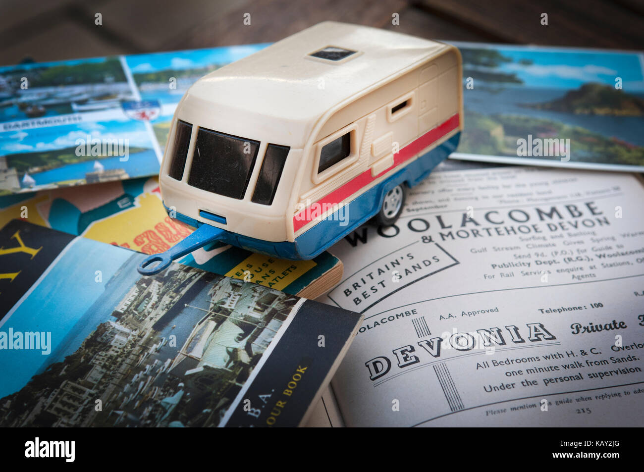 Plastica giocattolo il traino di caravan si siede su vintage holiday pubblicità per woolacombe nel Devon e colorate cartoline di mare. Stile anni '60 Foto Stock