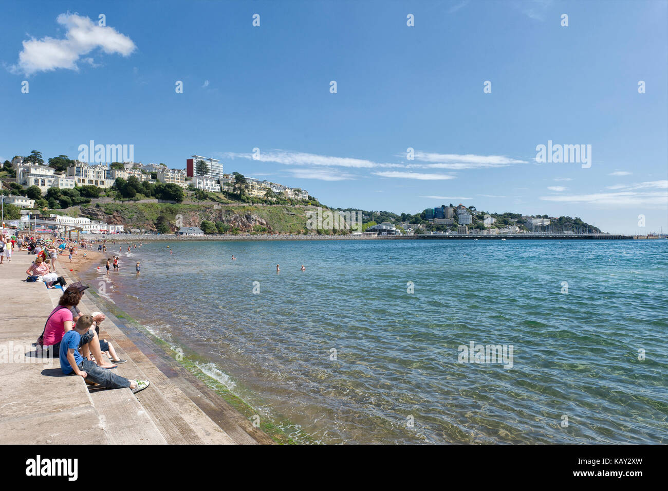 Una vacanza in famiglia a Torre Abbey Sands, Torquay, Devon, sedetevi sul lungomare ammirando la spiaggia e la vista della Baia di Tor in una soleggiata giornata estiva. Foto Stock