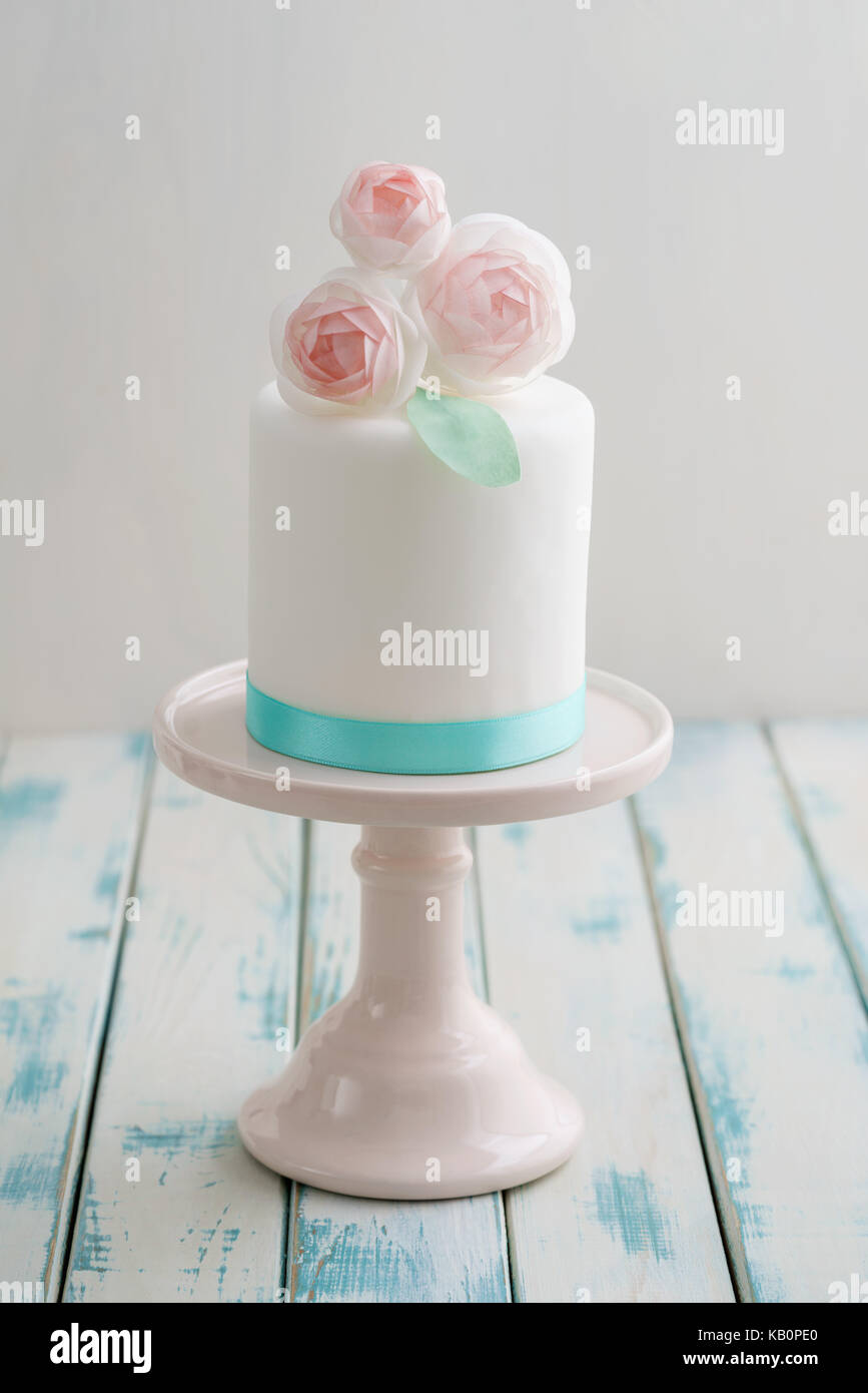 Mini bianco coperto fondente torta di nozze con carta di wafer ranunculus fiori sulla torta rosa stand con nastro turchese Foto Stock