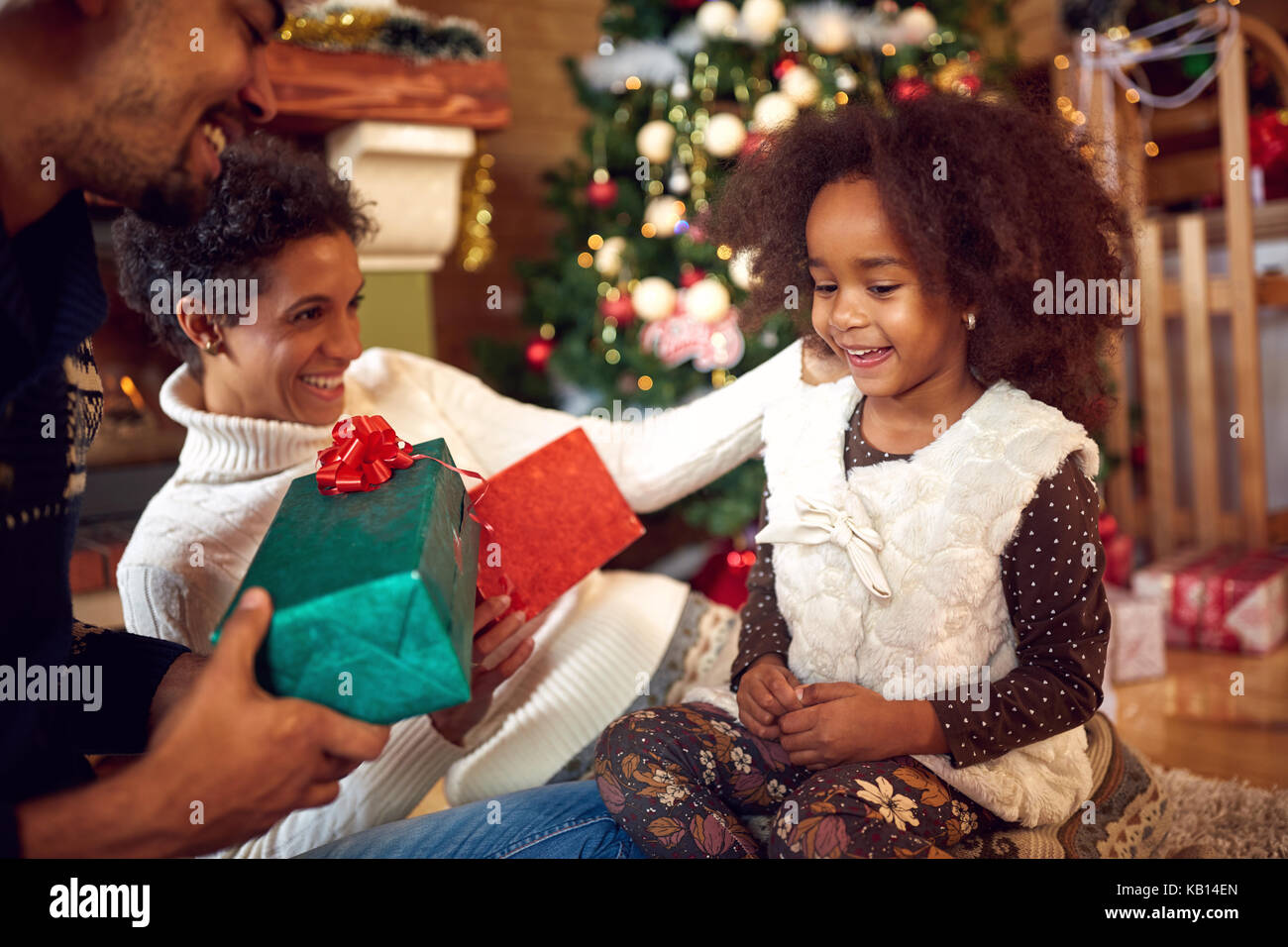 Bel bambino nero con i genitori e le caselle con i regali di Natale in casa Foto Stock