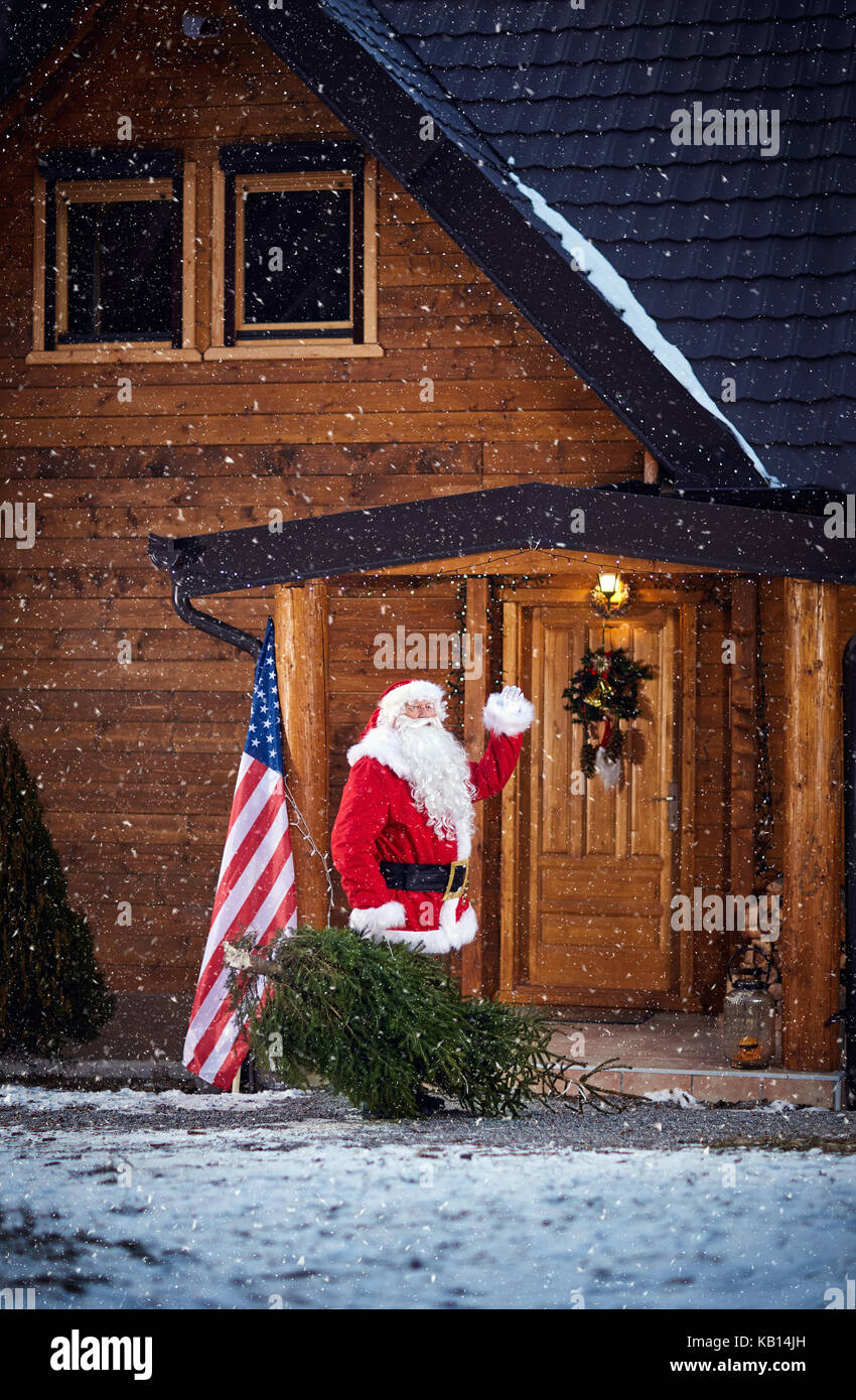Santa Claus sventolare quando entra nella casa di montagna con albero di natale Foto Stock