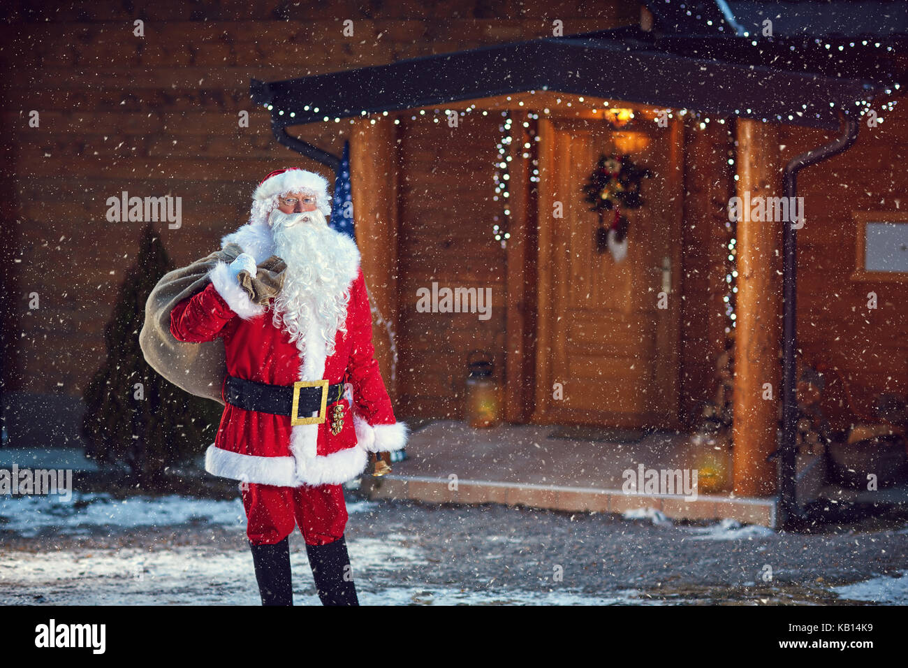 Babbo Natale con il sacco pieno di doni nella parte anteriore della casa in legno Foto Stock