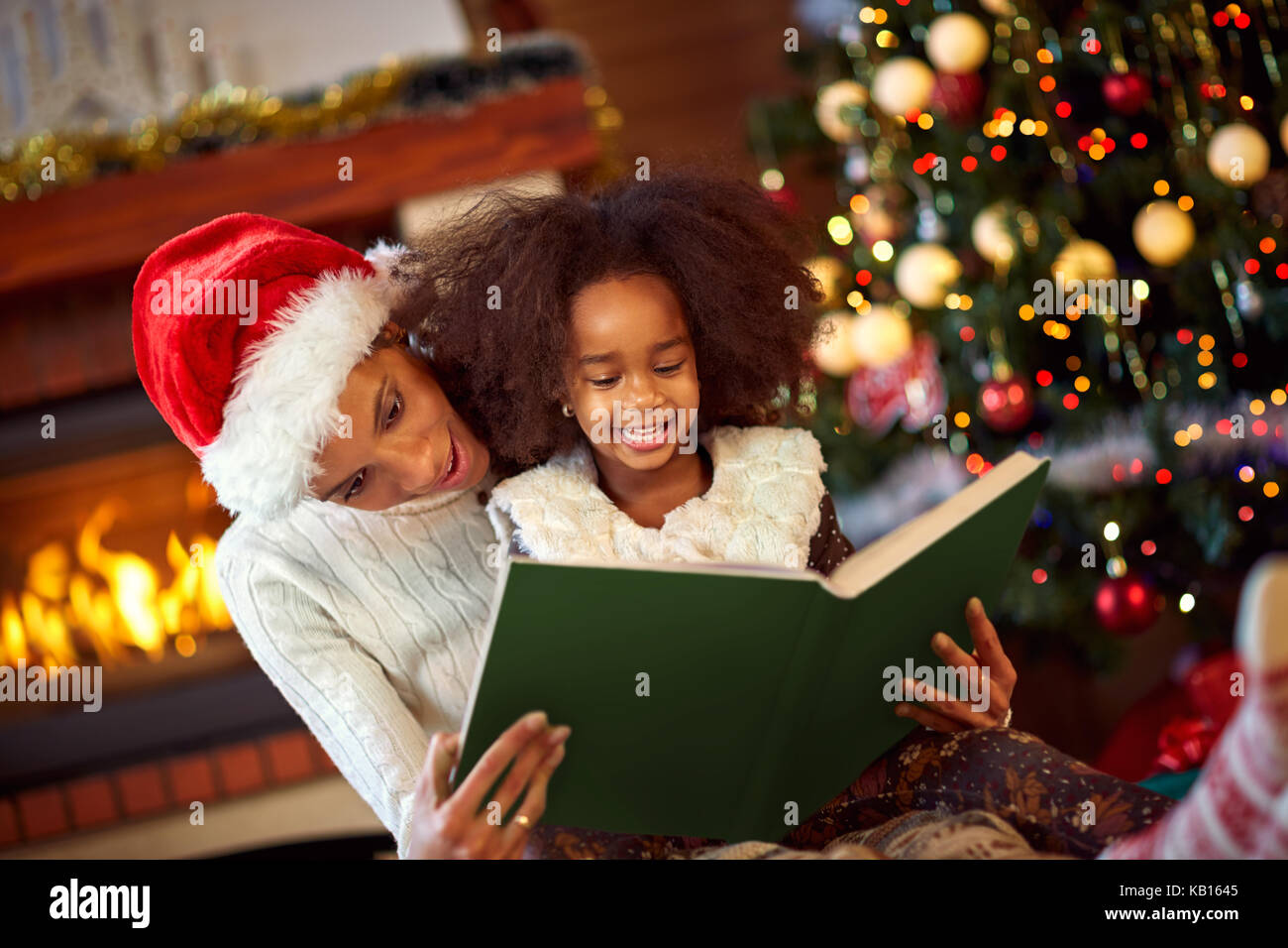 Piuttosto giovane madre la lettura di un libro a sua figlia vicino ad albero di Natale, buon natale Foto Stock