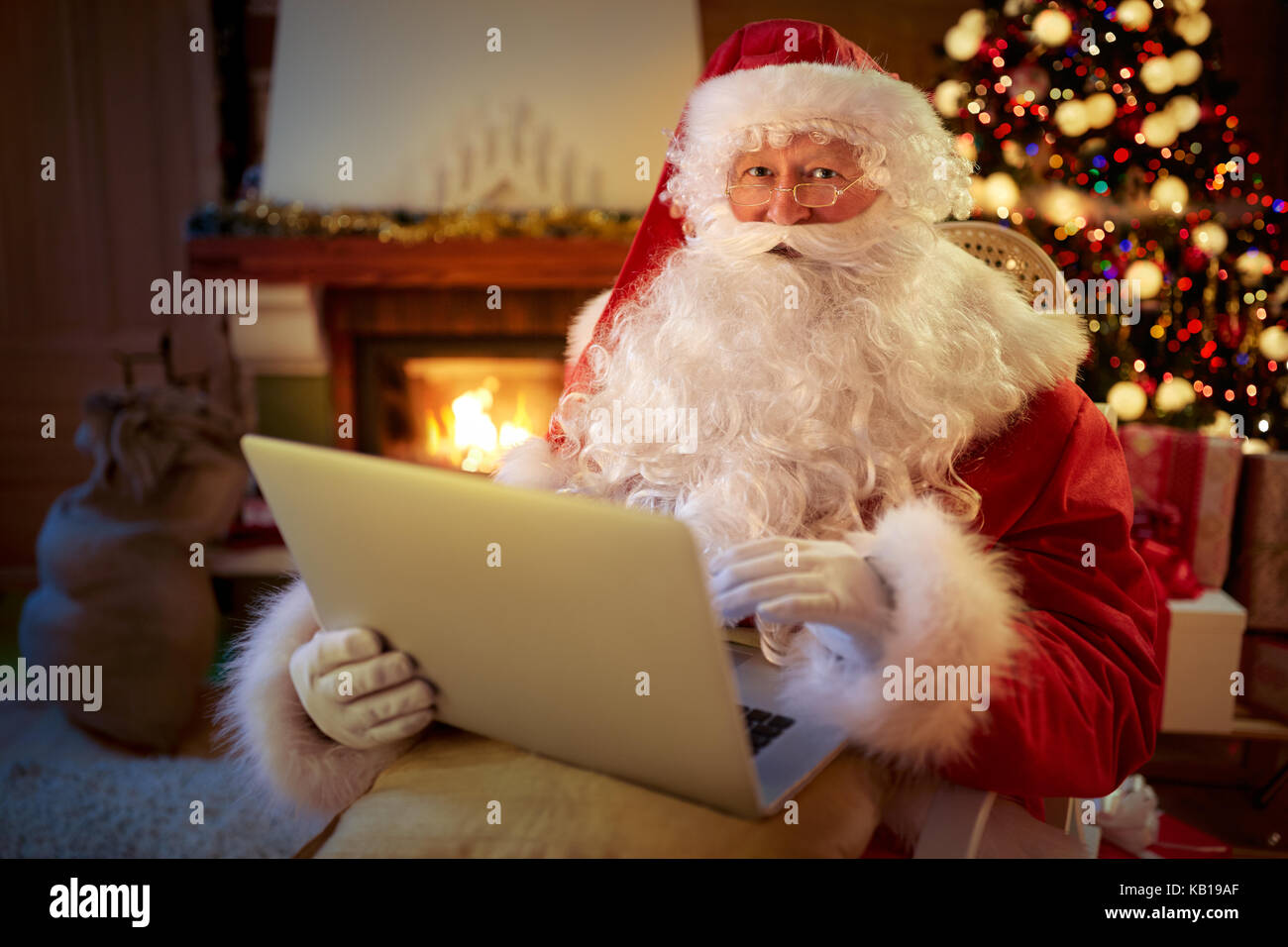 Babbo Natale seduti davanti al caminetto e la lettura della lettera di Natale o la lista dei desideri su laptop Foto Stock