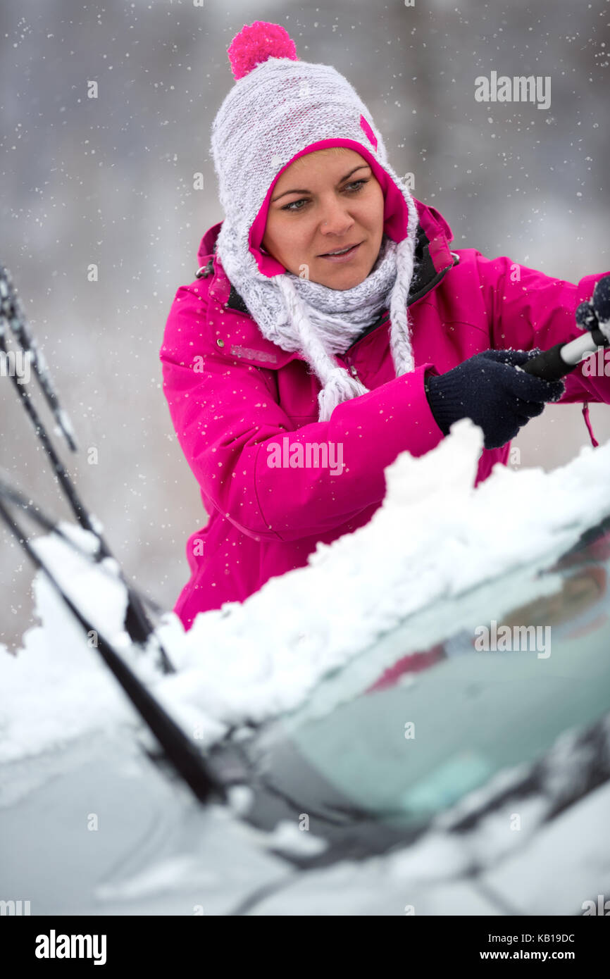 Ragazza giovane pulizia vetri auto da neve nella stagione invernale Foto Stock