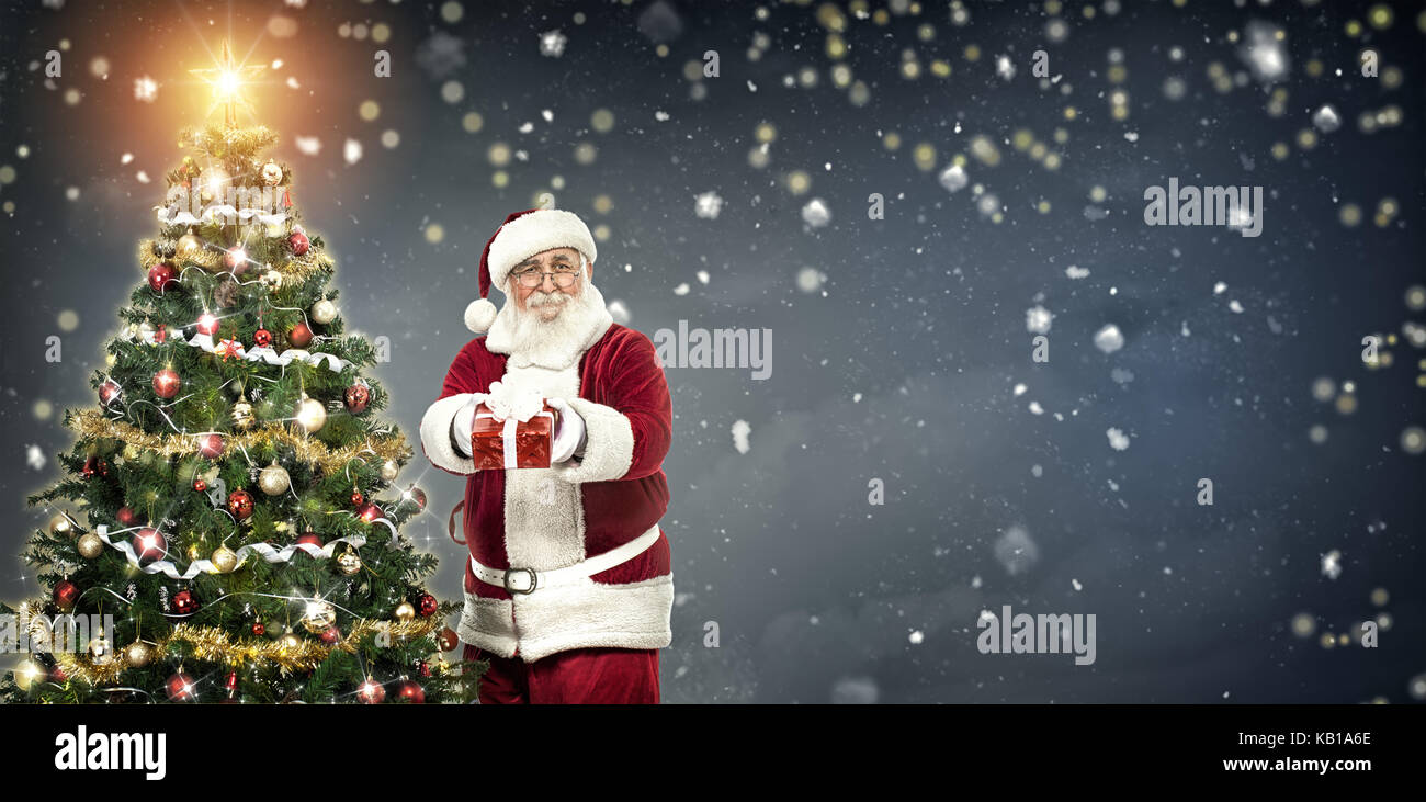 Babbo Natale regalo di contenimento e in piedi accanto ad albero di natale su sfondo inverno Foto Stock