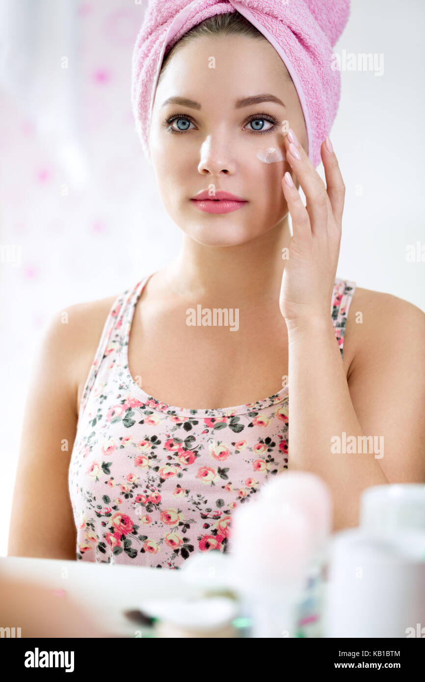Giovane ragazza in bagno lato anteriore dello specchio retrovisore mettendo la crema, dermocosmesi Foto Stock