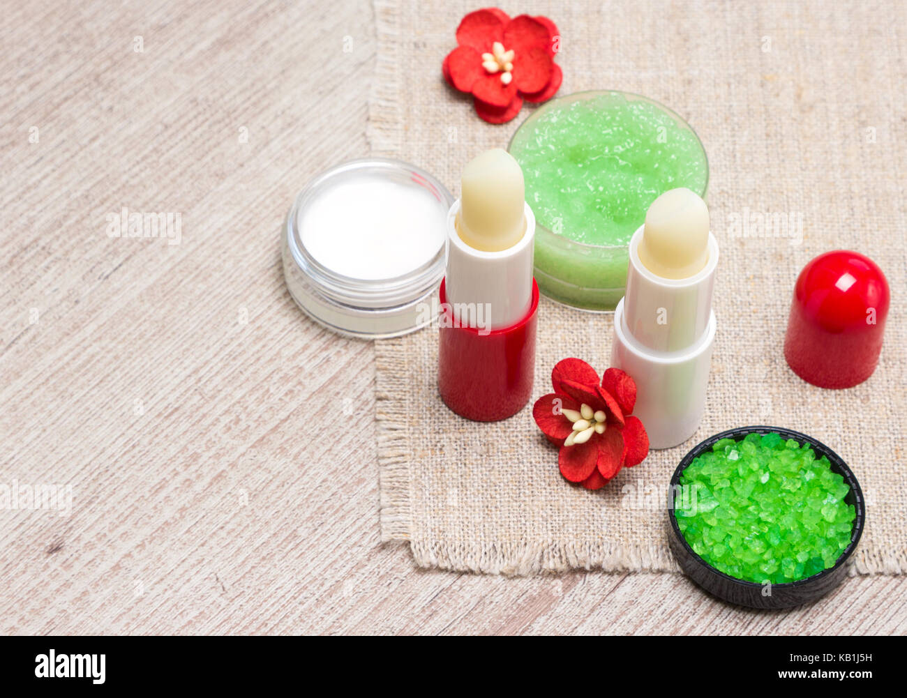 Prodotti cosmetici per labbro cura della pelle: sale marino, miele naturale macchia con oli essenziali, labbro balsami e crema con fiori sul malandato superficie in legno Foto Stock