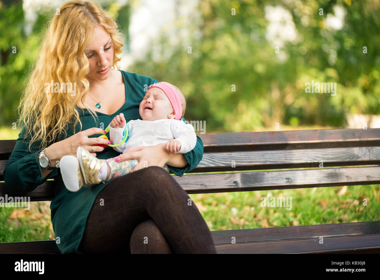 Mom lenisce il pianto di un bambino seduto su una panchina nel parco Foto Stock