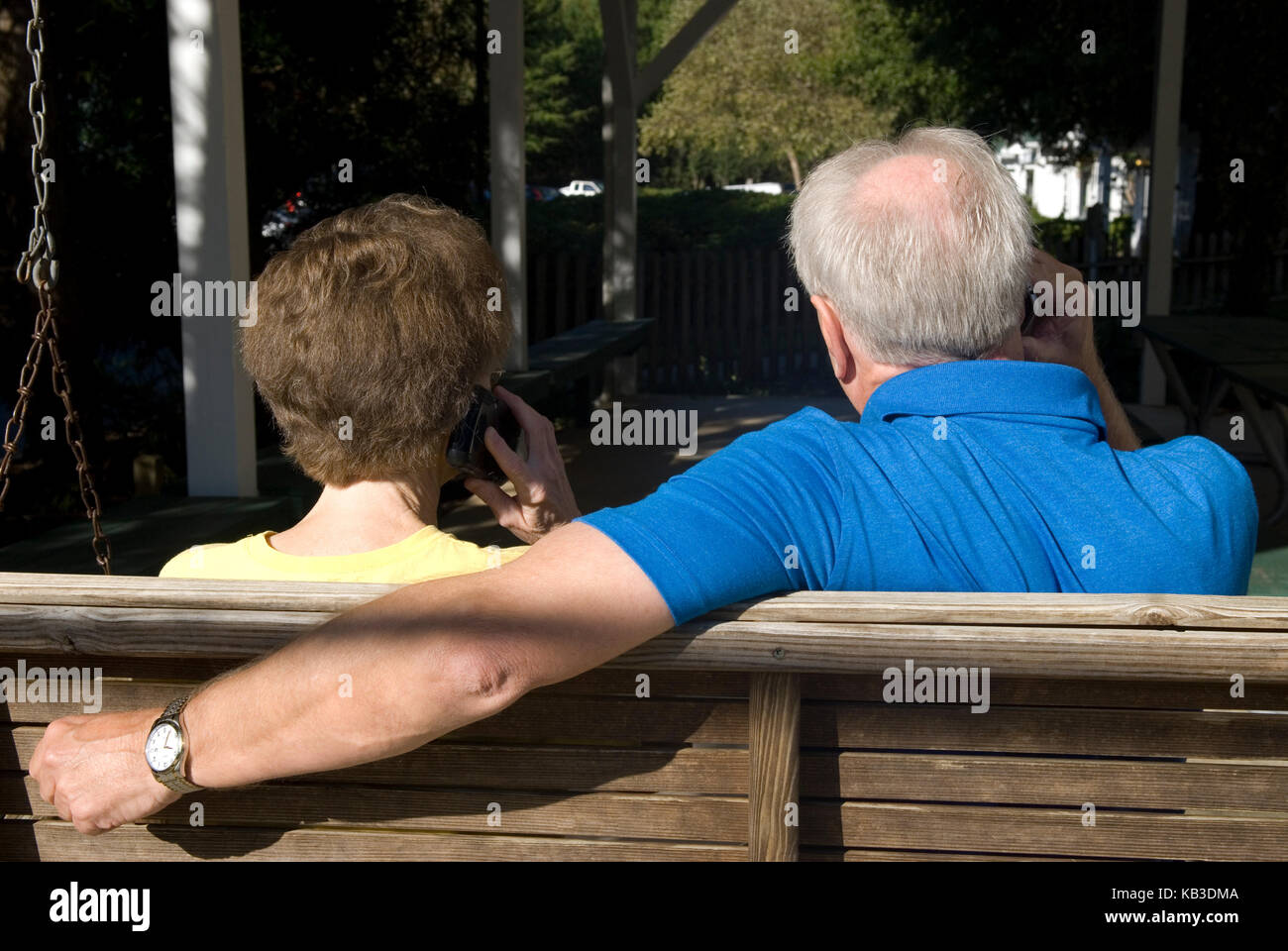Caucasian Senior Couple (età 60-70) in swing mentre parlano sul cellulare al complesso di appartamenti, Stati Uniti Foto Stock Caucasian Senior Couple (età 60-70) in swing mentre parlano sul cellulare al complesso di appartamenti, Stati Uniti Foto Stock