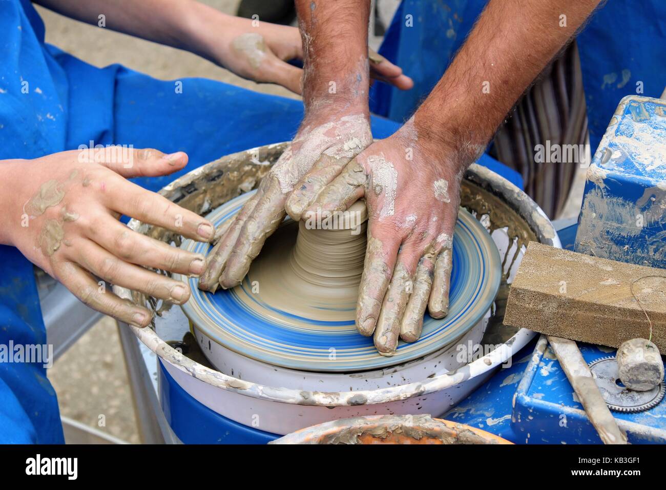 Gli uomini hanno le mani sul tornio del vasaio e le mani del suo pupillo sono nelle vicinanze. Foto Stock