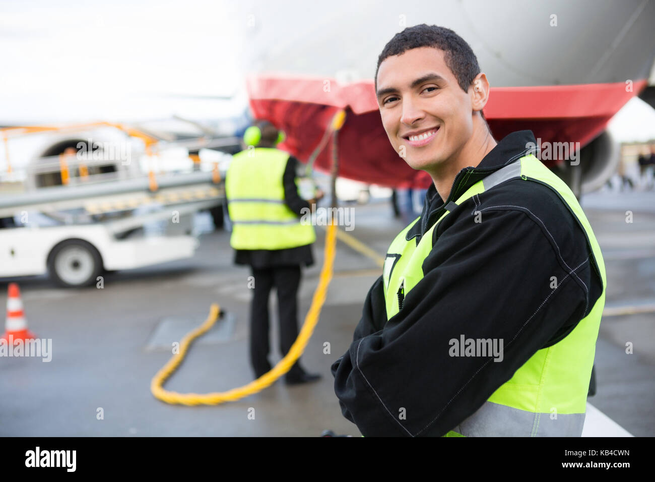 Ritratto di fiducia lavoratore maschile sorridere mentre aereo essendo caricato in pista Foto Stock