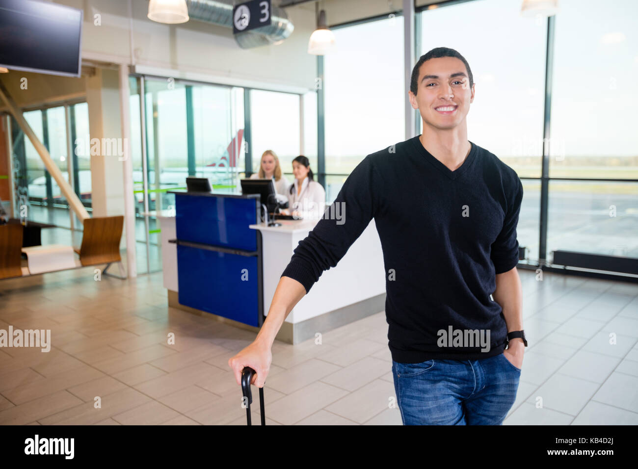 Ritratto di giovane sorridente passeggero maschio con receptionist in background in aeroporto Foto Stock