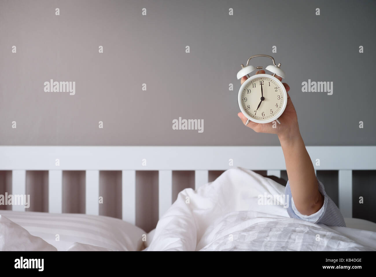 La mano sotto la coperta si estende alla sveglia al mattino con la luce arancione. Foto Stock